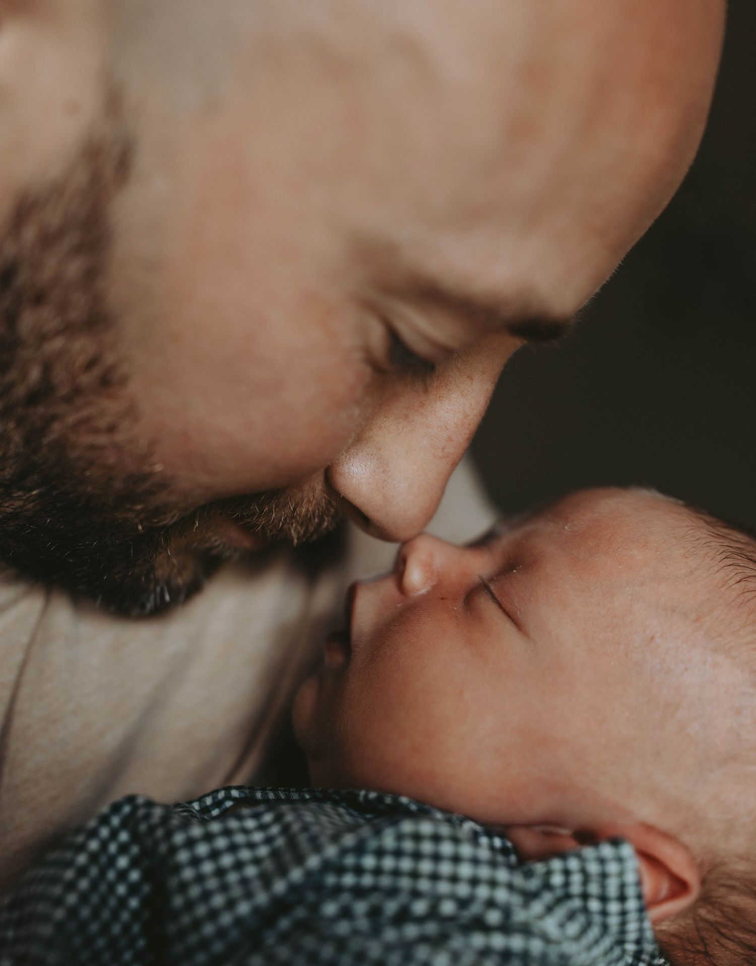 Bearded father gently kissing his newborn baby on the nose.