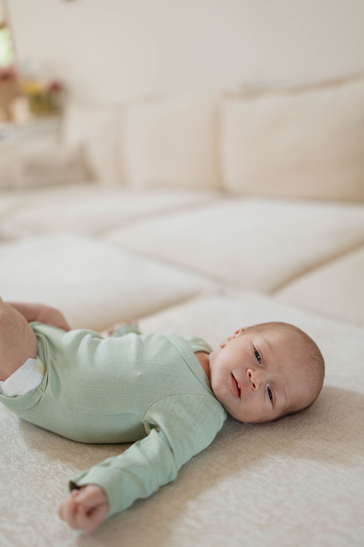 An infant lies on a cream-colored blanket in a mint green onesie showing different angles of their resting position.
