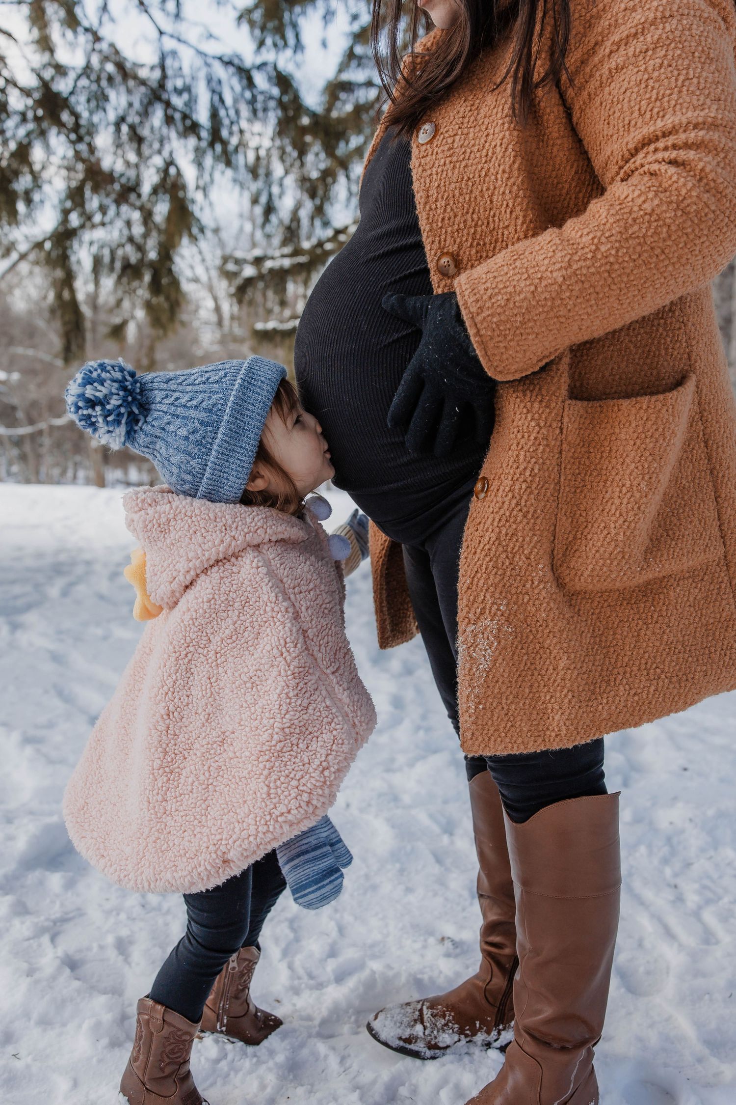 A touching winter moment between parent and child wearing cozy coats and boots while standing in the snow.