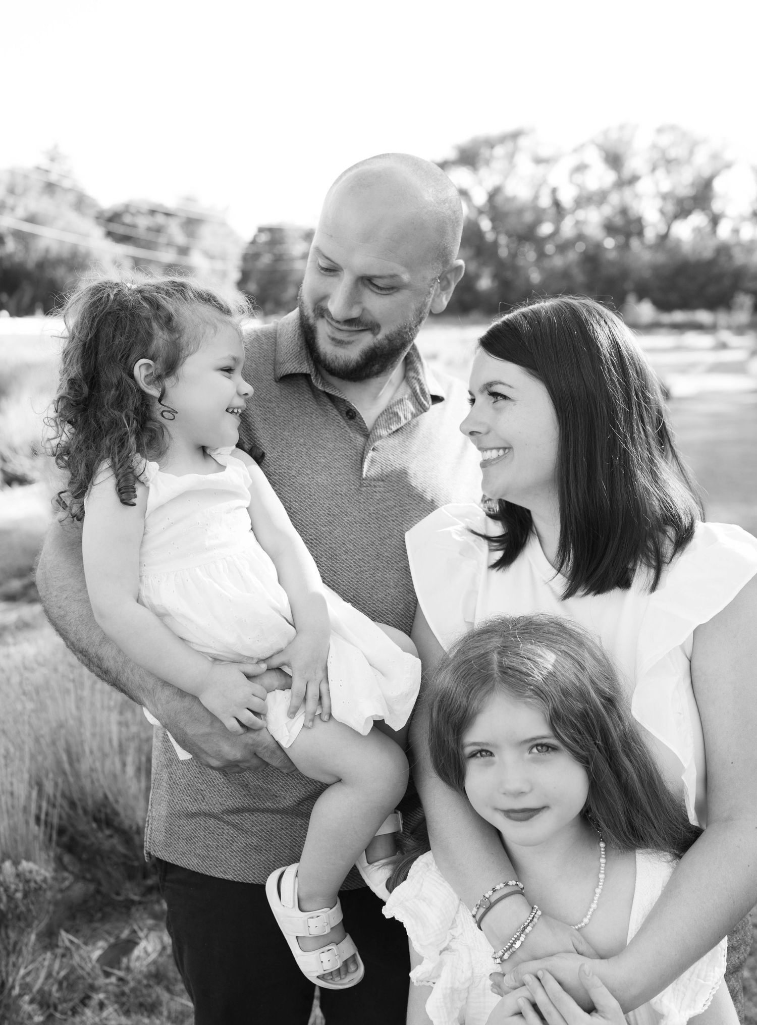 A black and white portrait of a family of four standing together outdoors in a natural setting.