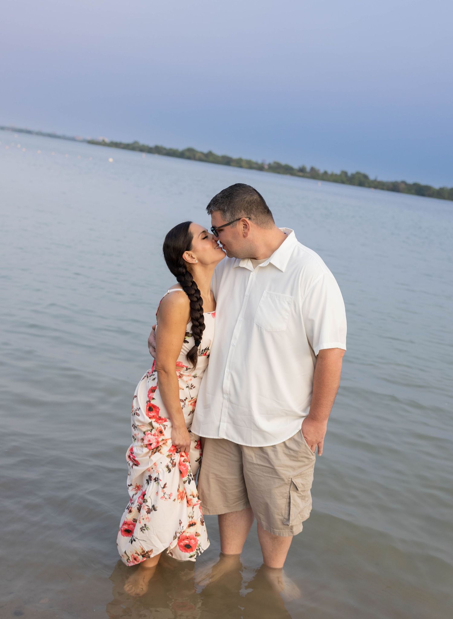 Couple sharing a romantic kiss while standing in shallow water at the beach, wearing casual summer attire.