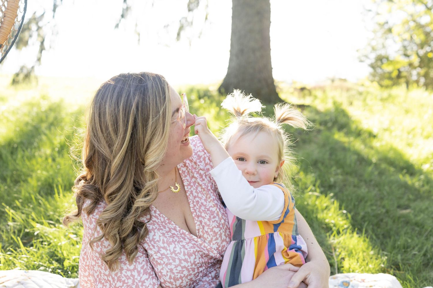 A pink floral dress and colorful rainbow dress contrast beautifully against a sunny green outdoor setting.