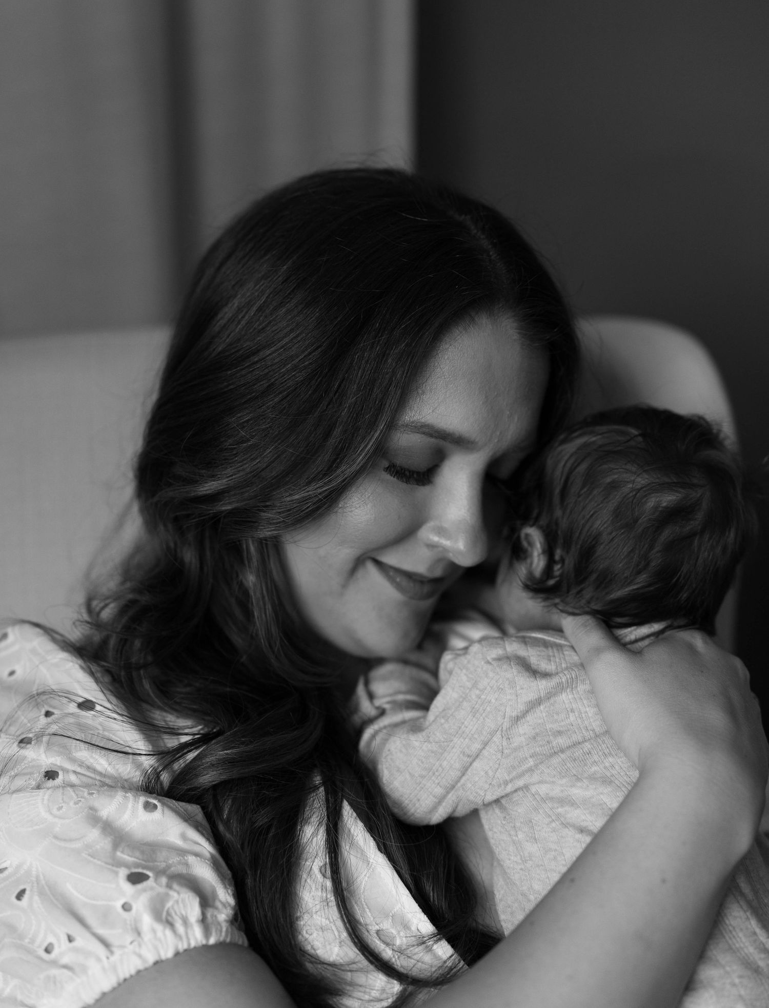 Black and white photo of a smiling mother tenderly holding her newborn baby close to her face.
