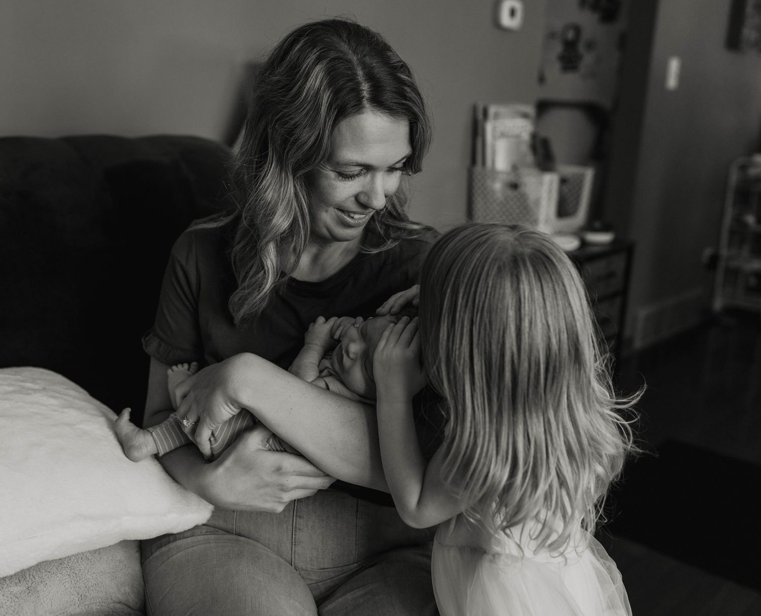 Black and white photo of a smiling mother sitting with her young blonde daughter in a cozy home setting.