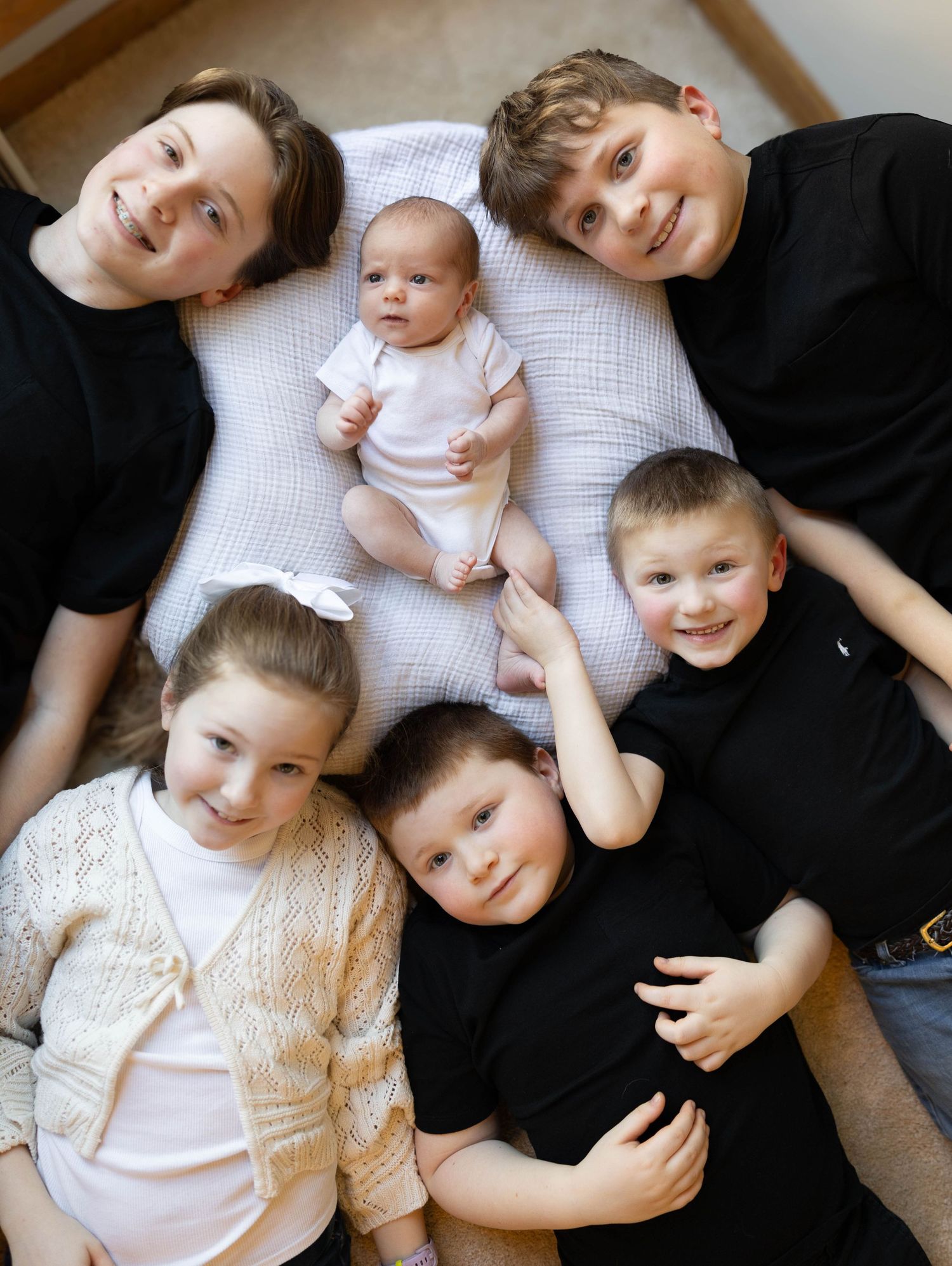 A group lies together on a white surface while wearing casual clothing in an intimate family portrait setup.