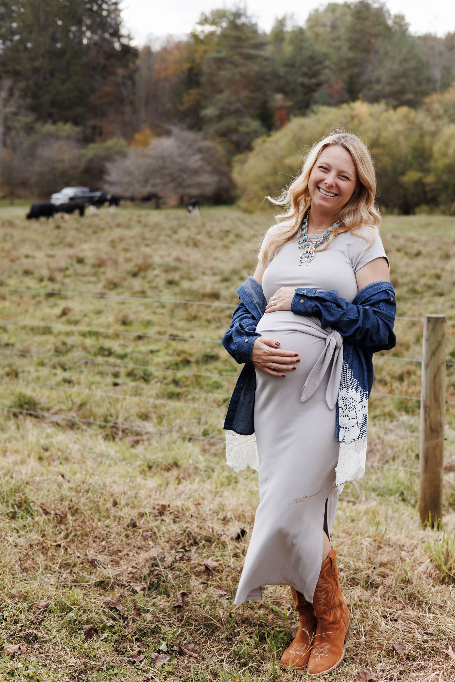 A maternity photoshoot in a rustic field setting with casual denim and brown boots.