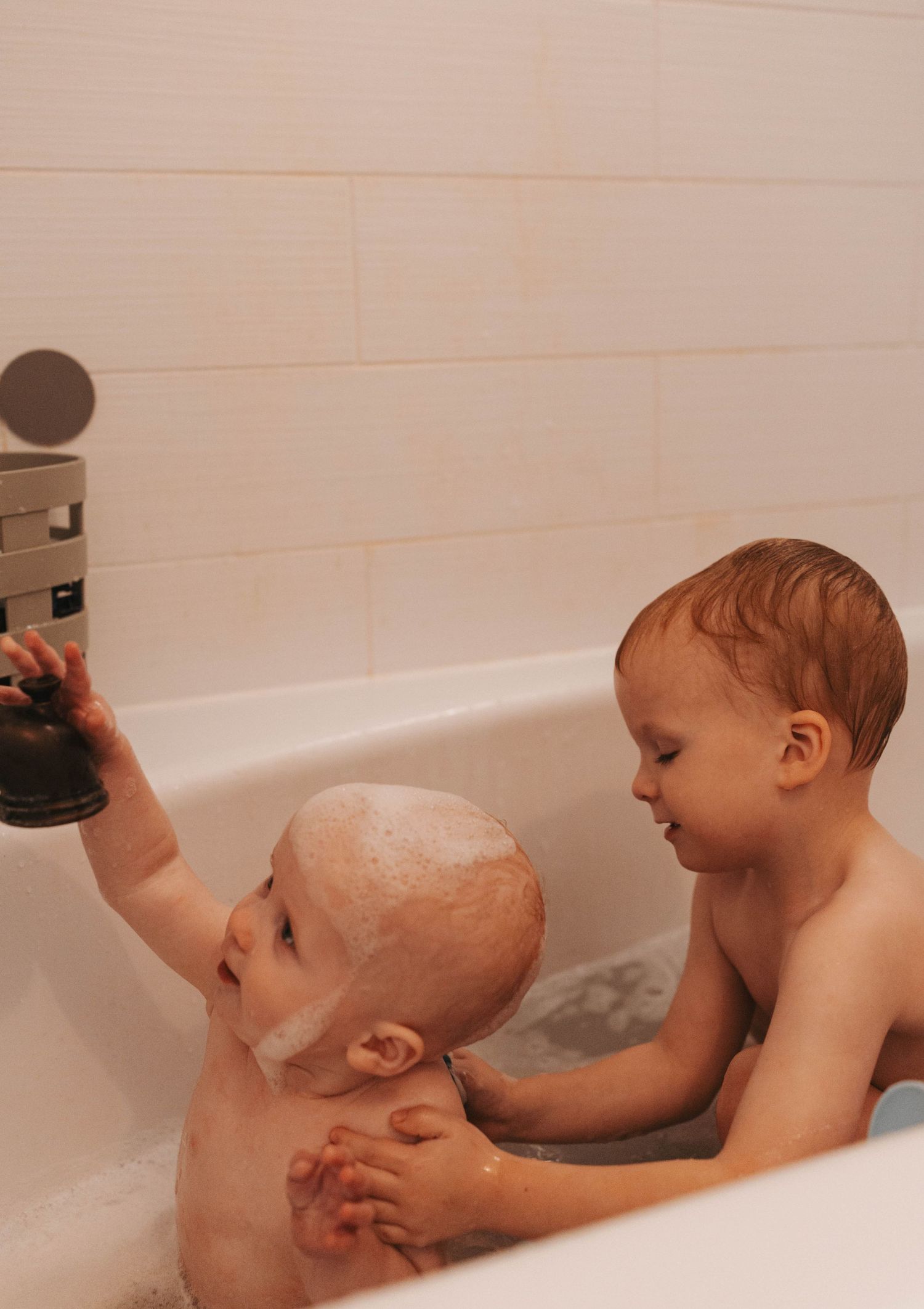 Baby splashing and playing during bathtime in white bathtub with water spraying.