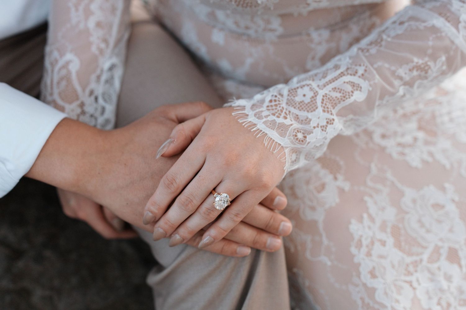 Close up detail of hands wearing an engagement ring with delicate lace fabric in the background.