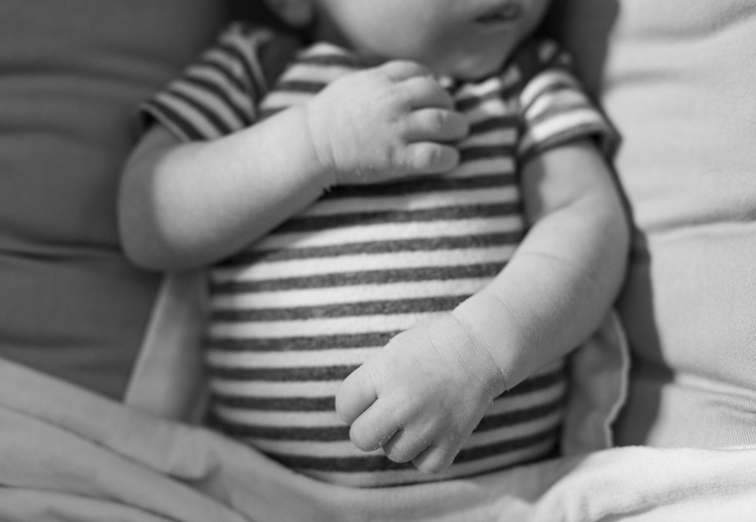 A black and white photo of a small infant's hands and legs resting on soft blankets or fabric.