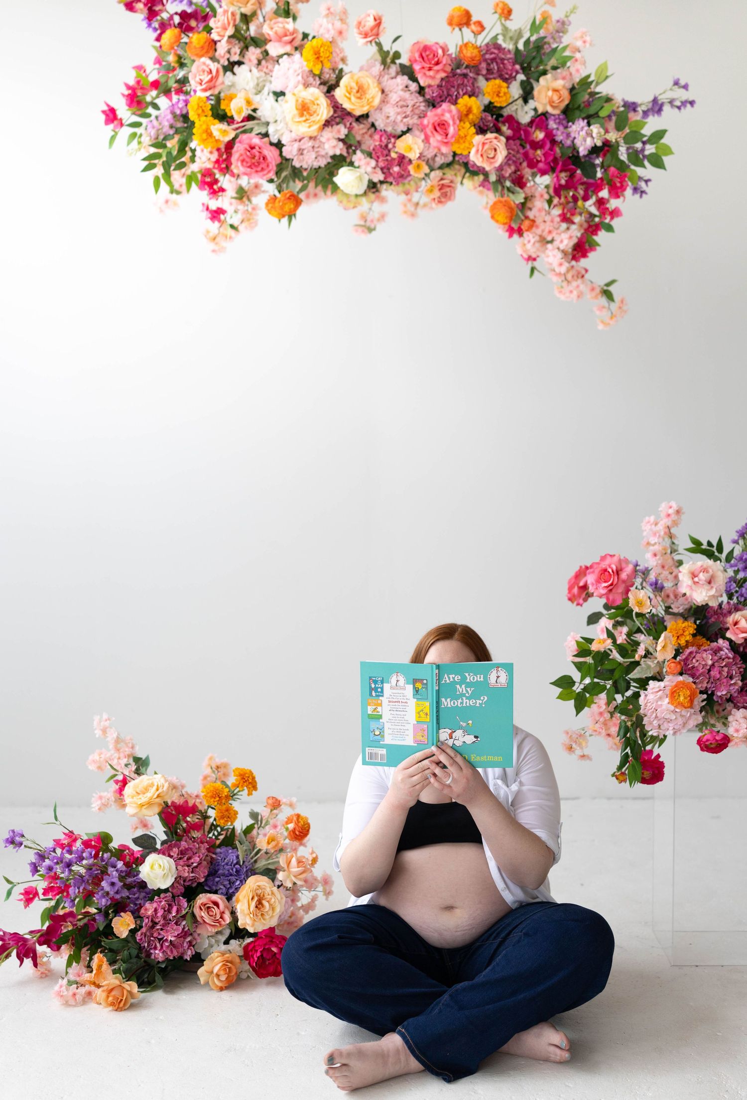 Vibrant floral arrangement with pink, orange and purple blooms frames a reading scene with maternity book on white backdrop.