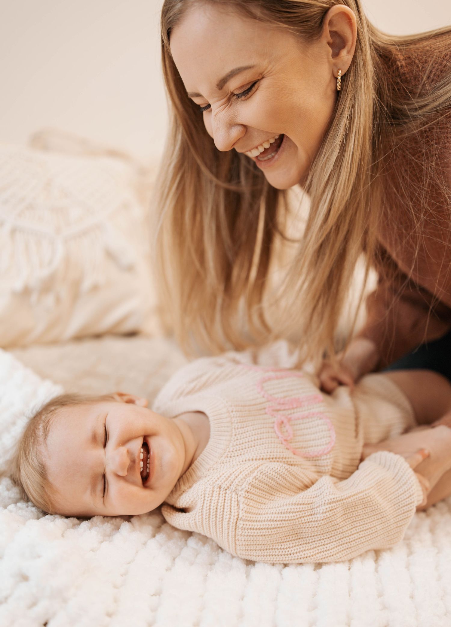 A tender moment shared between parent and child playing together on a white bedspread, filled with joyful laughter.