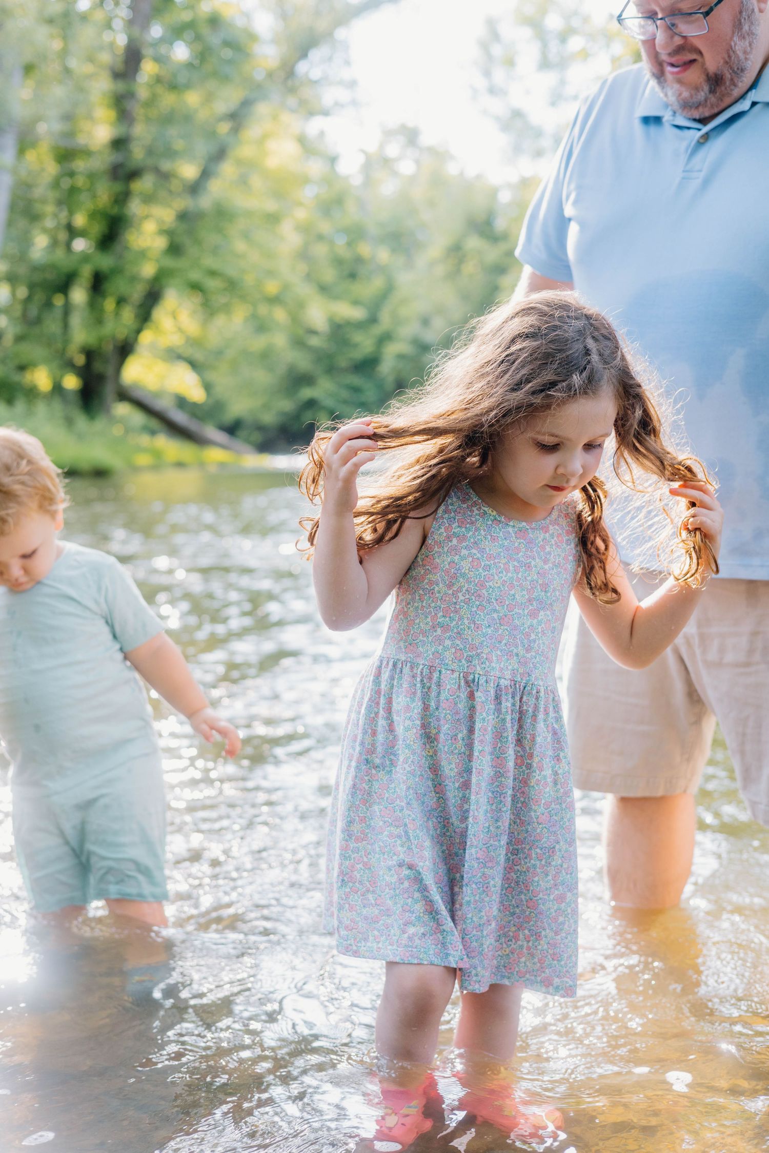 A grandfather wades in a shallow creek with two young children on a sunny summer day.