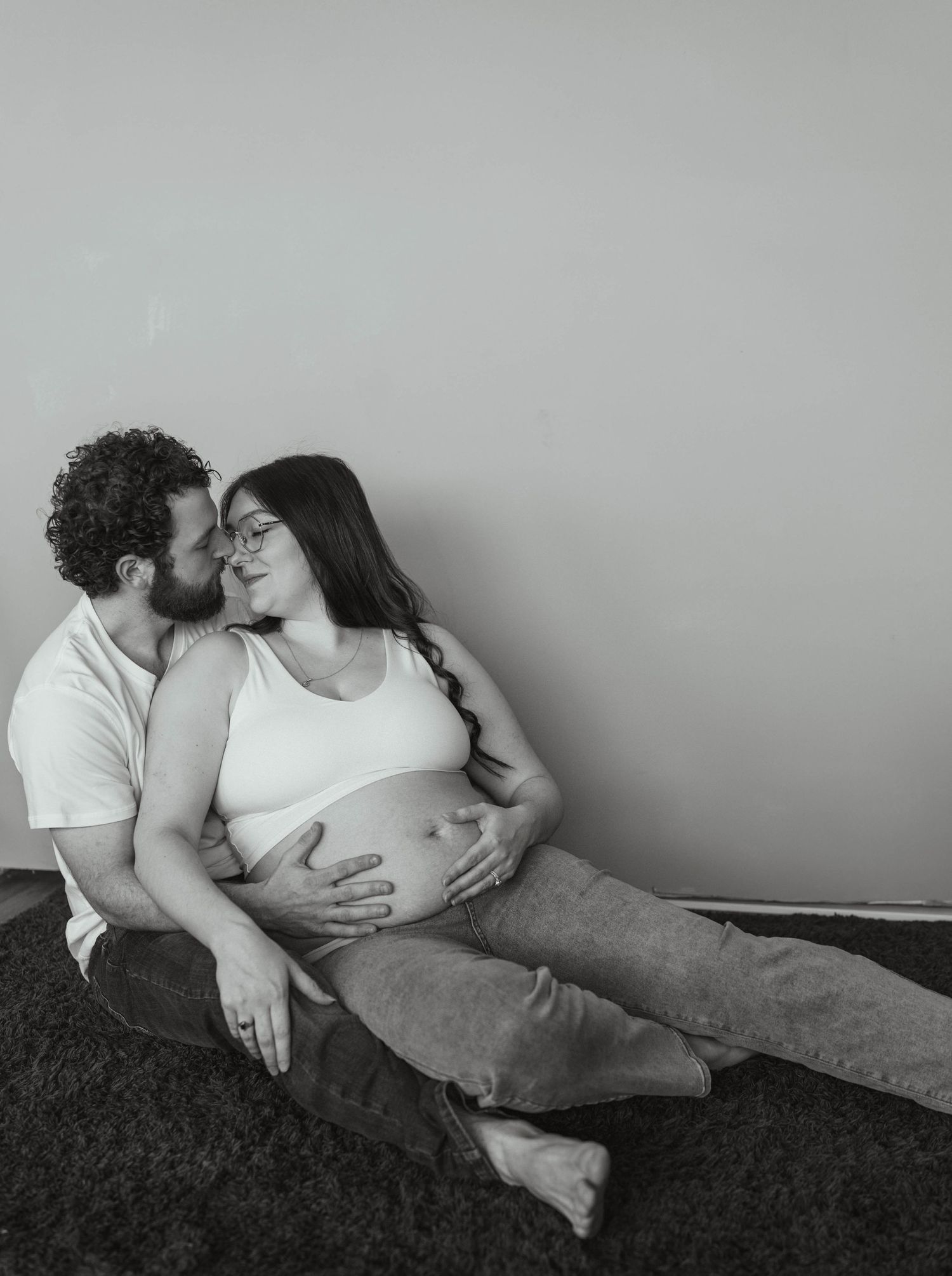A couple shares an intimate moment while resting on a dark blanket as they await their new arrival.