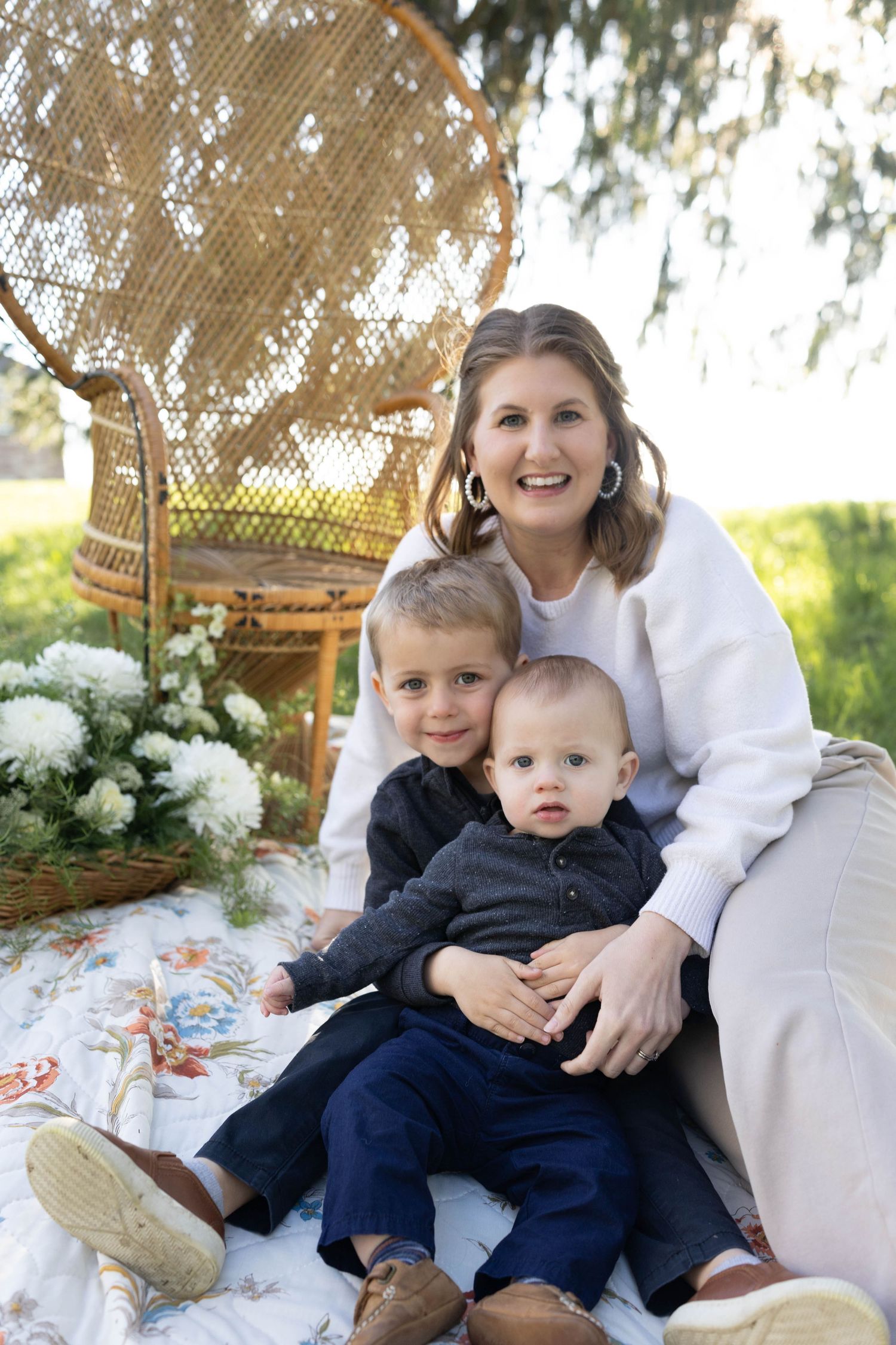 Outdoor family portrait on a blanket with decorative wicker furniture and white hydrangeas in the background.