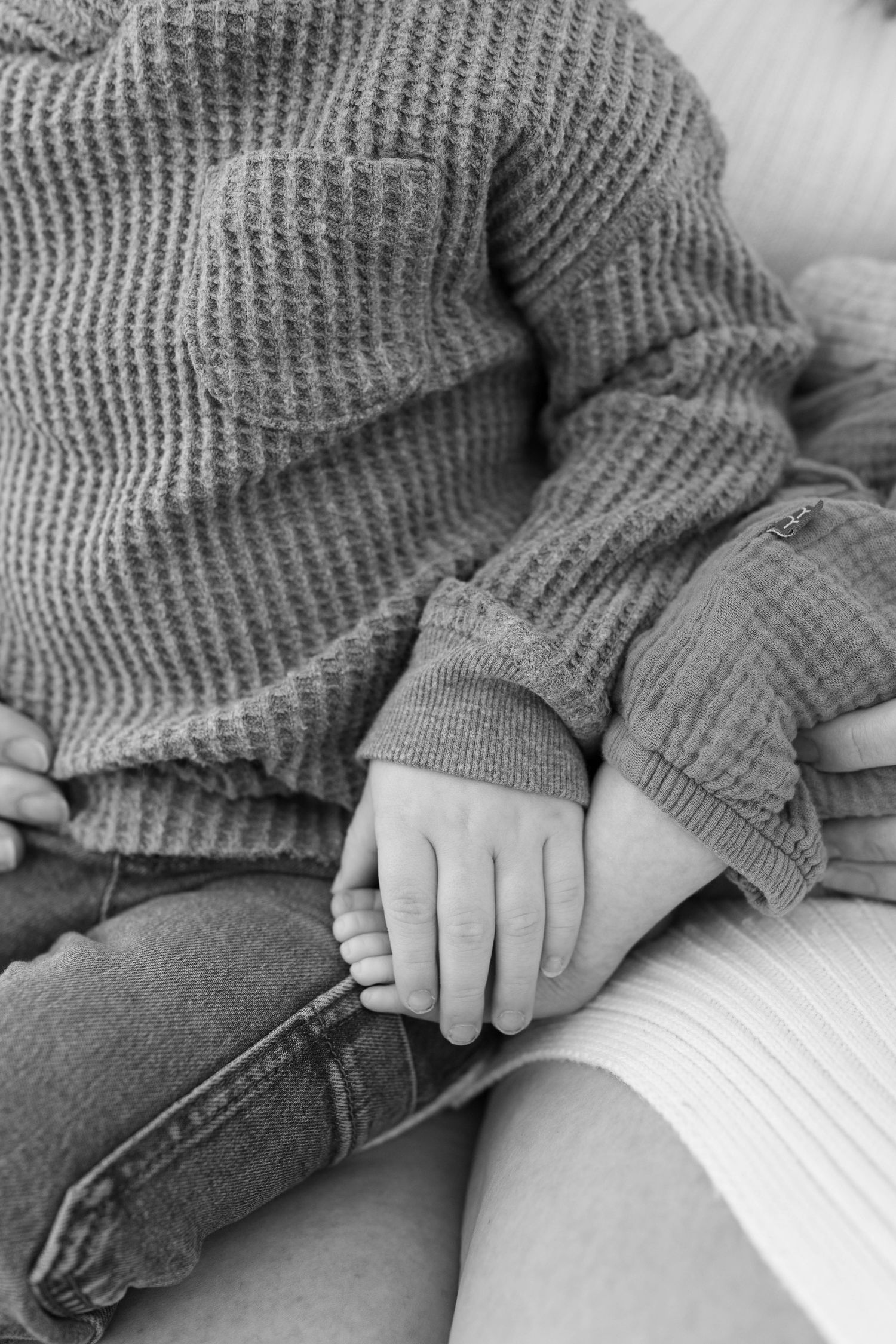 Black and white close up of hands clasped together while wearing a knit sweater and jeans.