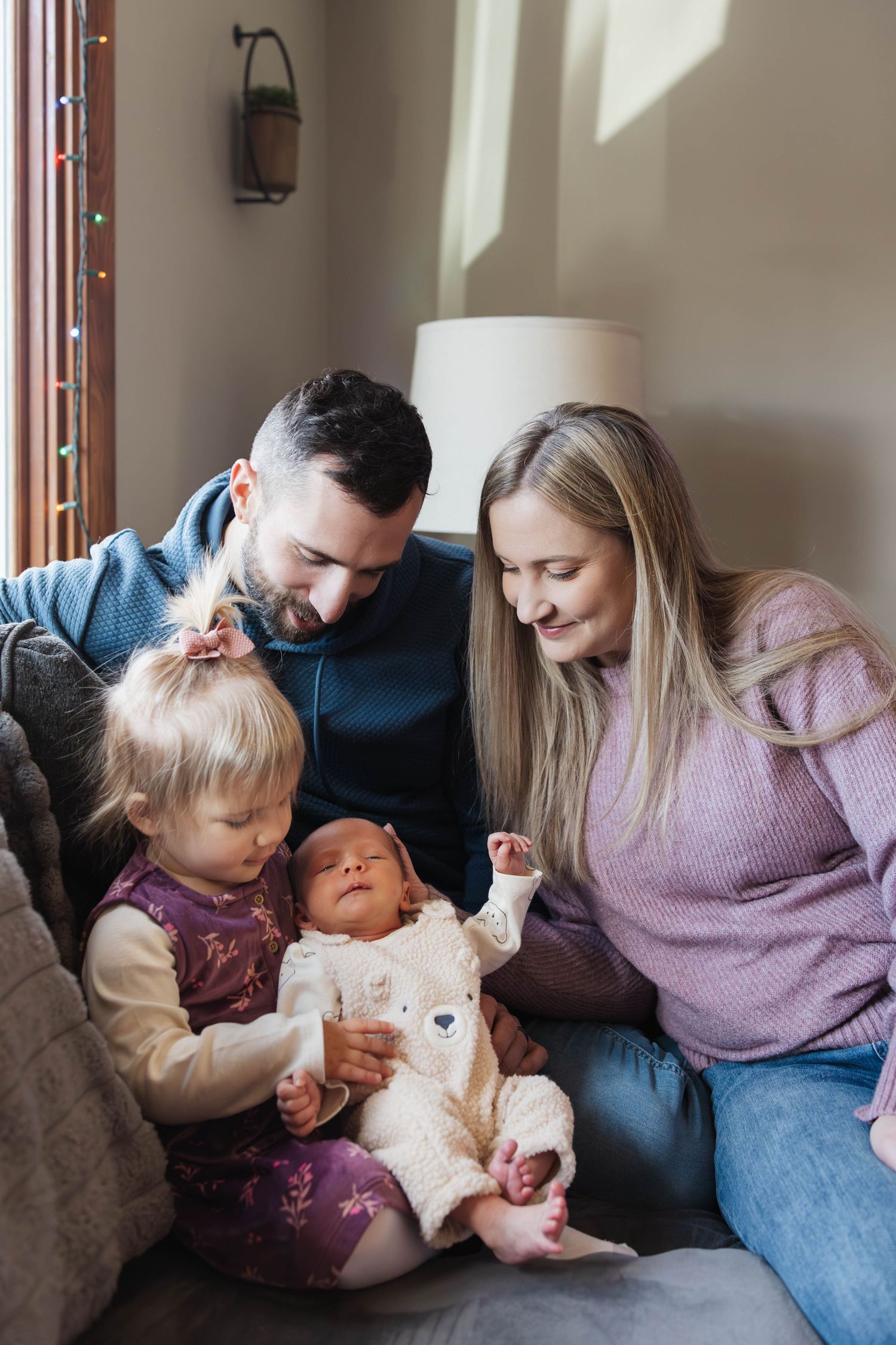 A family sits together on a couch, sharing a tender moment with their young children at home.