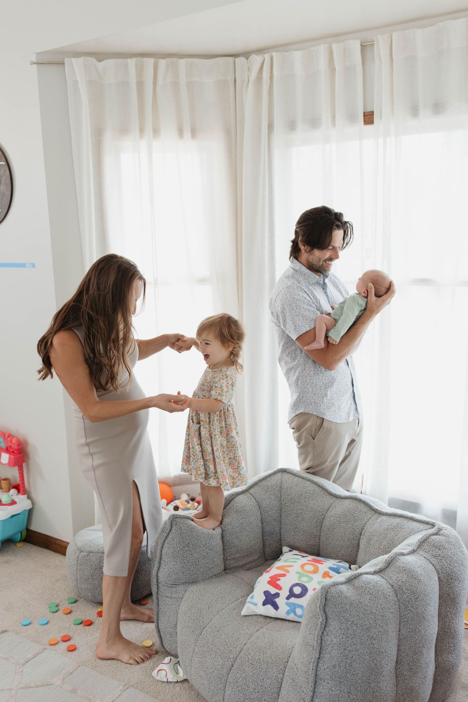 Family playing together in a bright living room with a grey couch and white curtains.