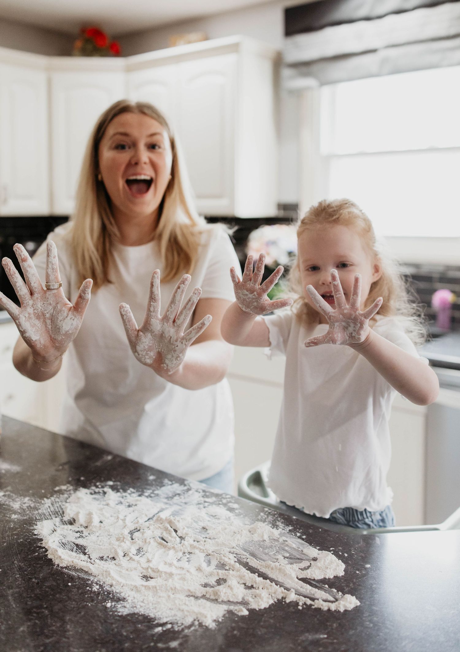 Two people having fun baking together in a kitchen while showing off their flour-covered hands and laughing.
