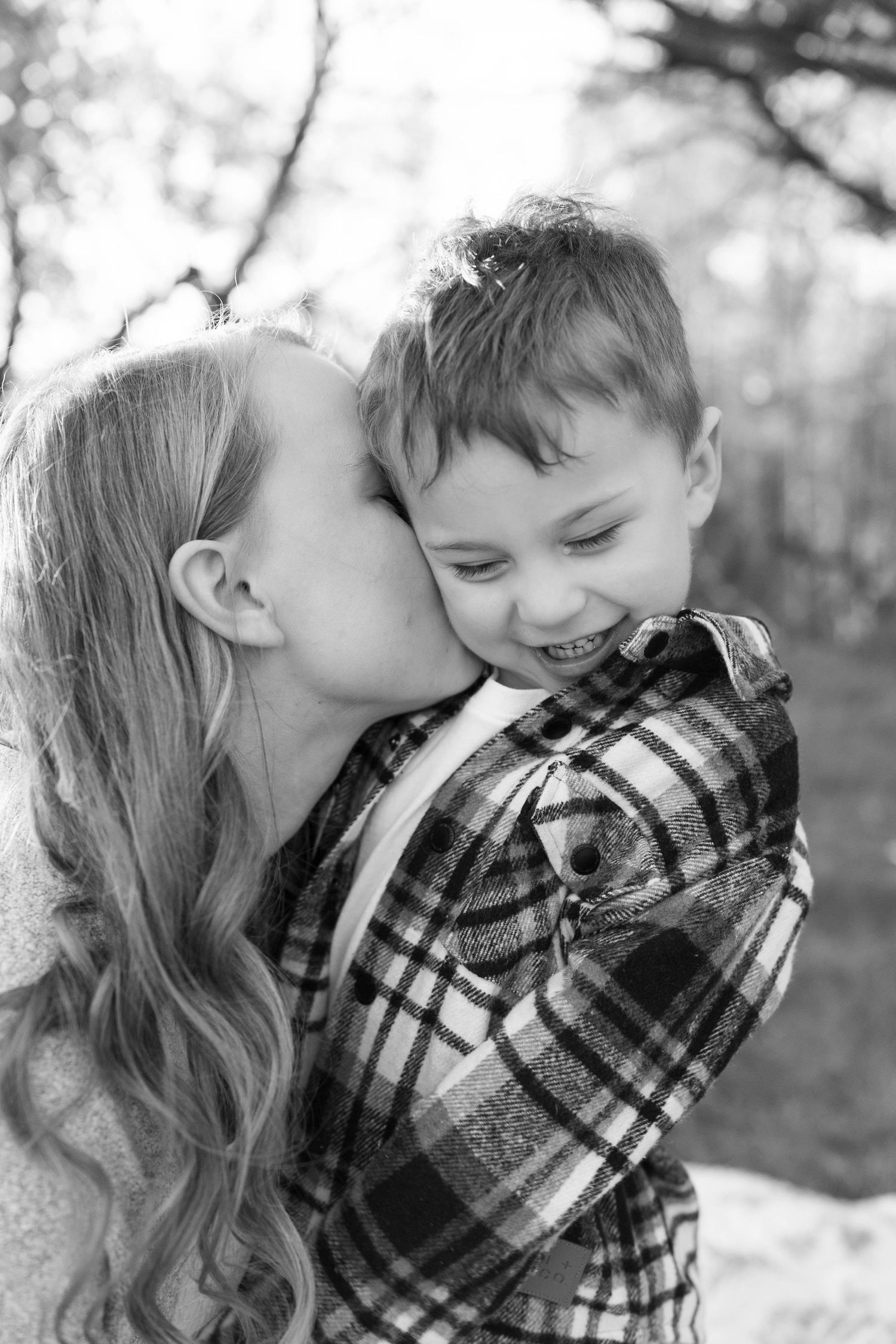Capturing a sweet moment between two young children in a black and white photograph as one gives a kiss to another.