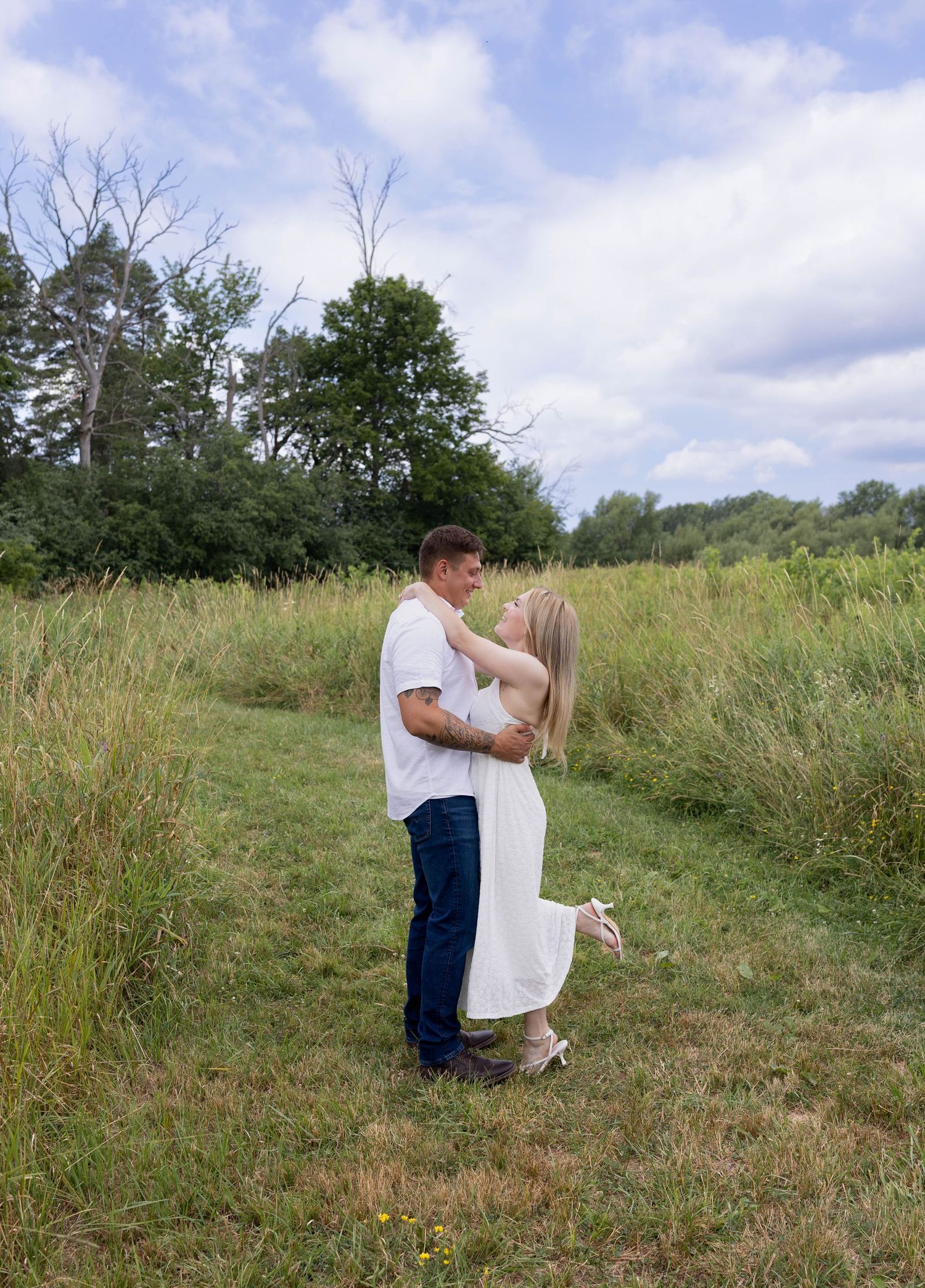 Couple sharing a kiss while dancing together on a grassy path surrounded by tall green fields.