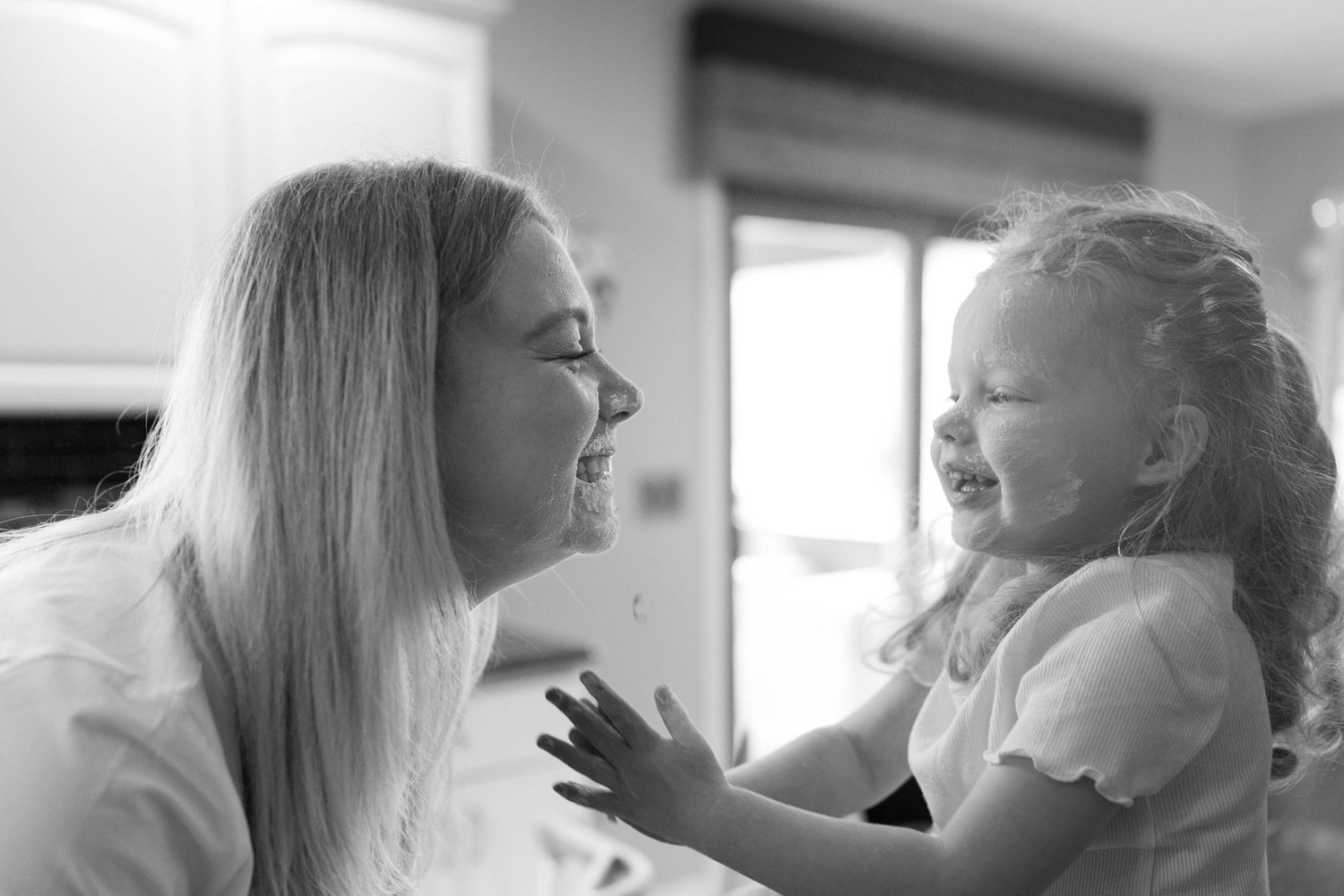 Black and white capture of a tender moment between parent and child laughing together indoors.