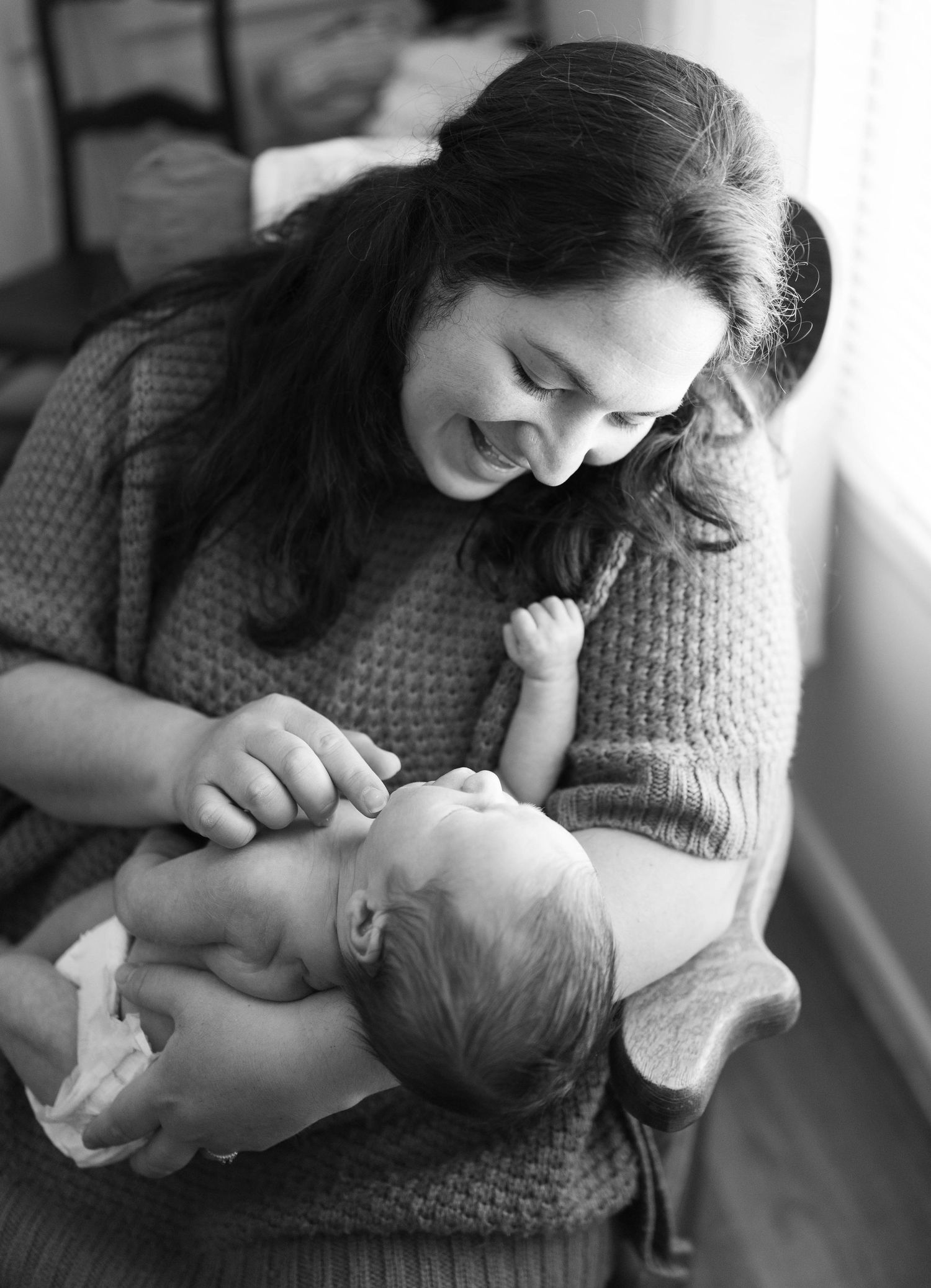Parent in a cozy sweater sharing an intimate bonding moment with their newborn baby in black and white.