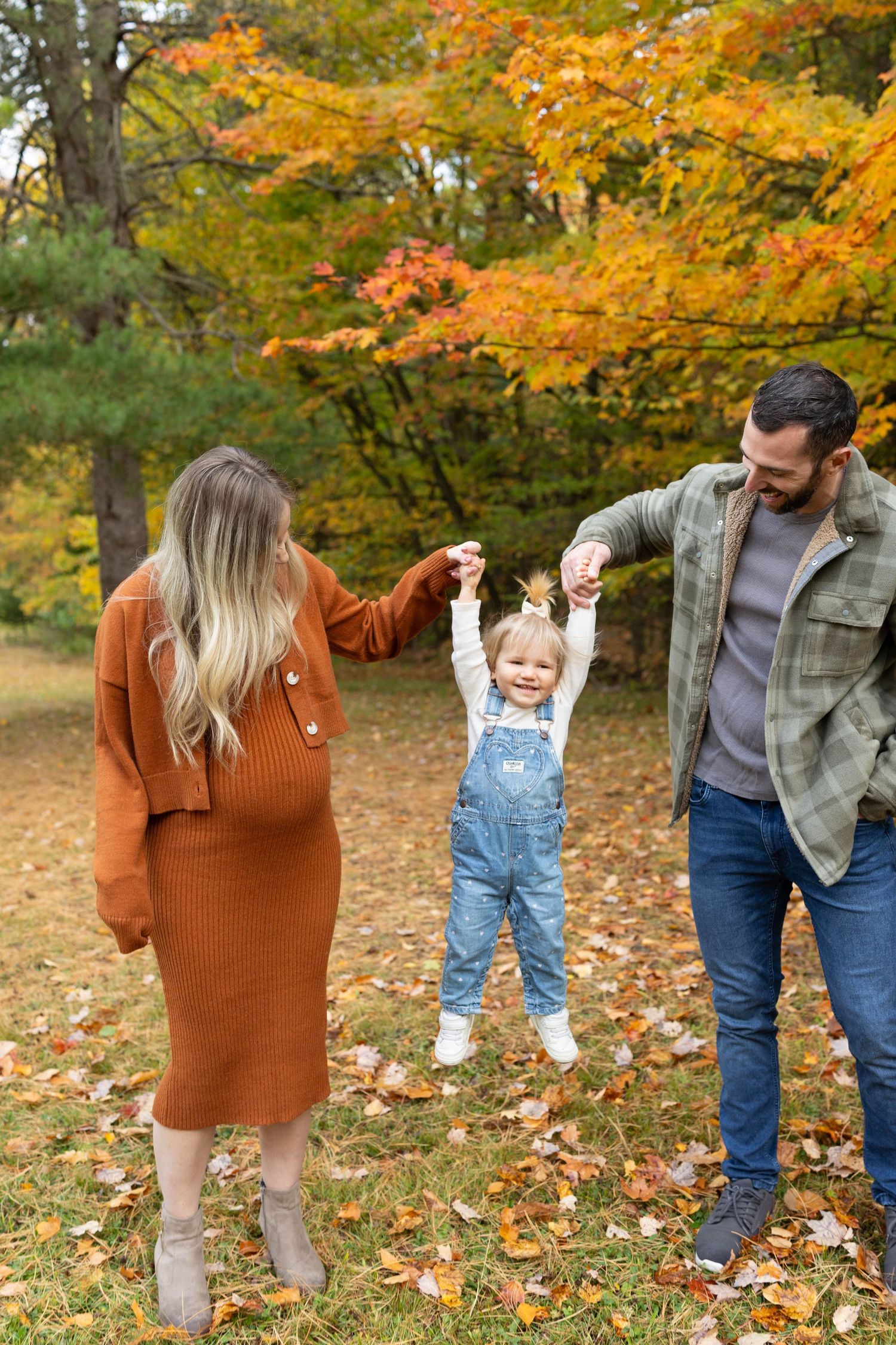 A family enjoys a playful autumn moment together among fallen orange leaves in a park setting.