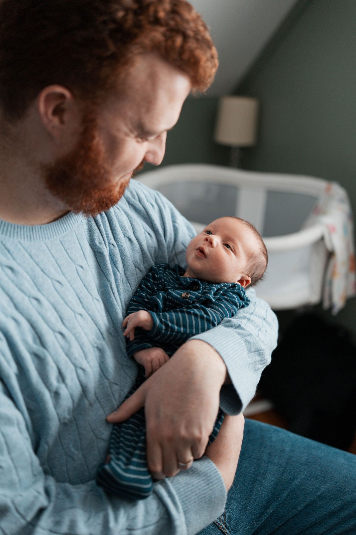 A tender moment captured as a parent in a blue sweater cradles a small newborn baby wearing a striped outfit.