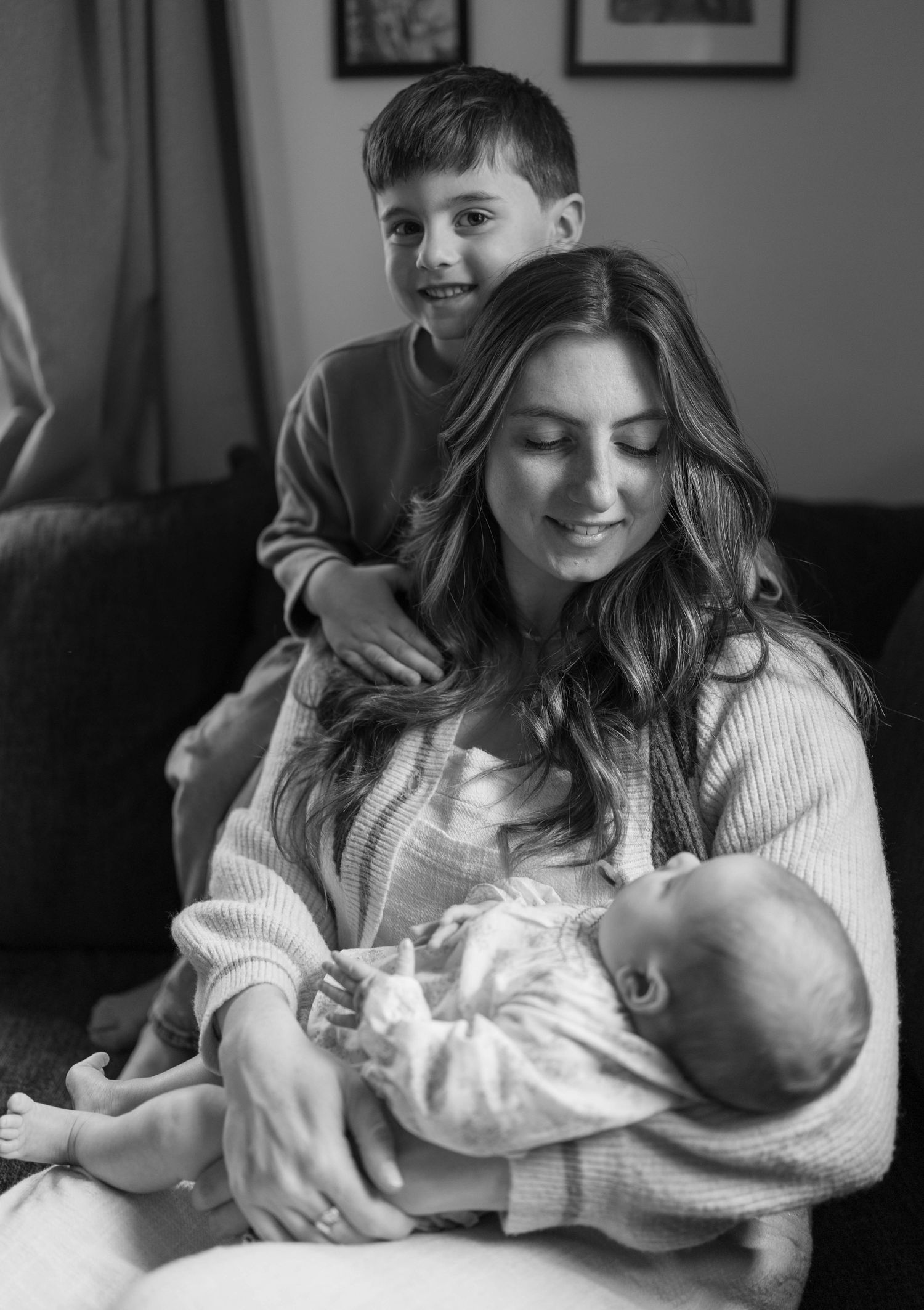 A tender black and white family portrait showing intimate bonding moments on a couch with a baby.