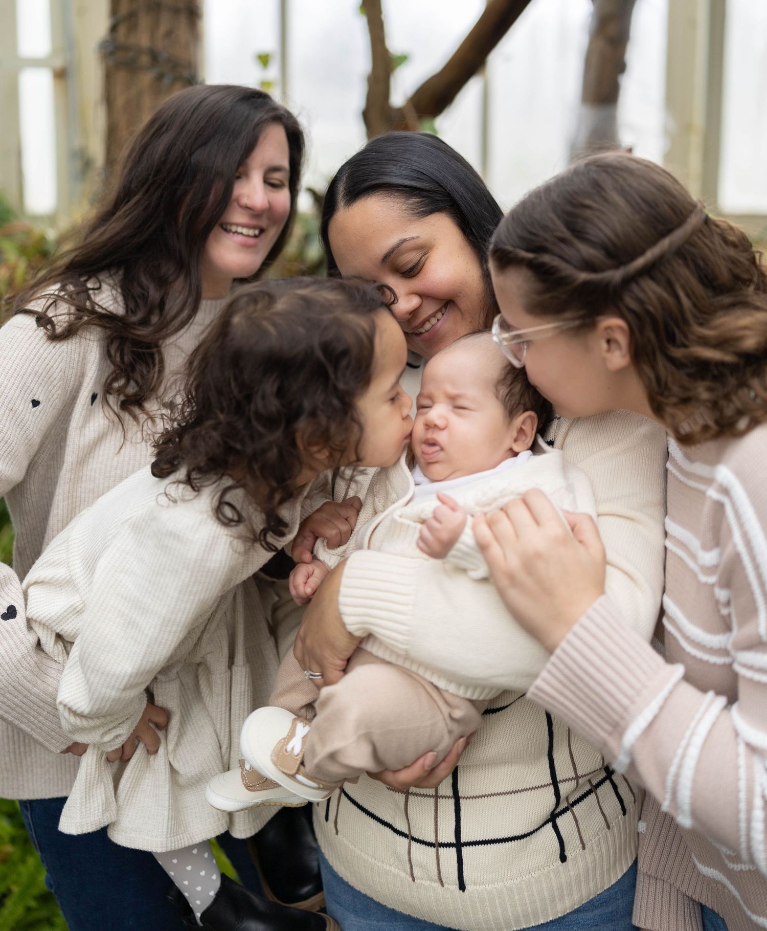 A small group huddles together affectionately around a baby in white sweaters on a winter day outdoors.