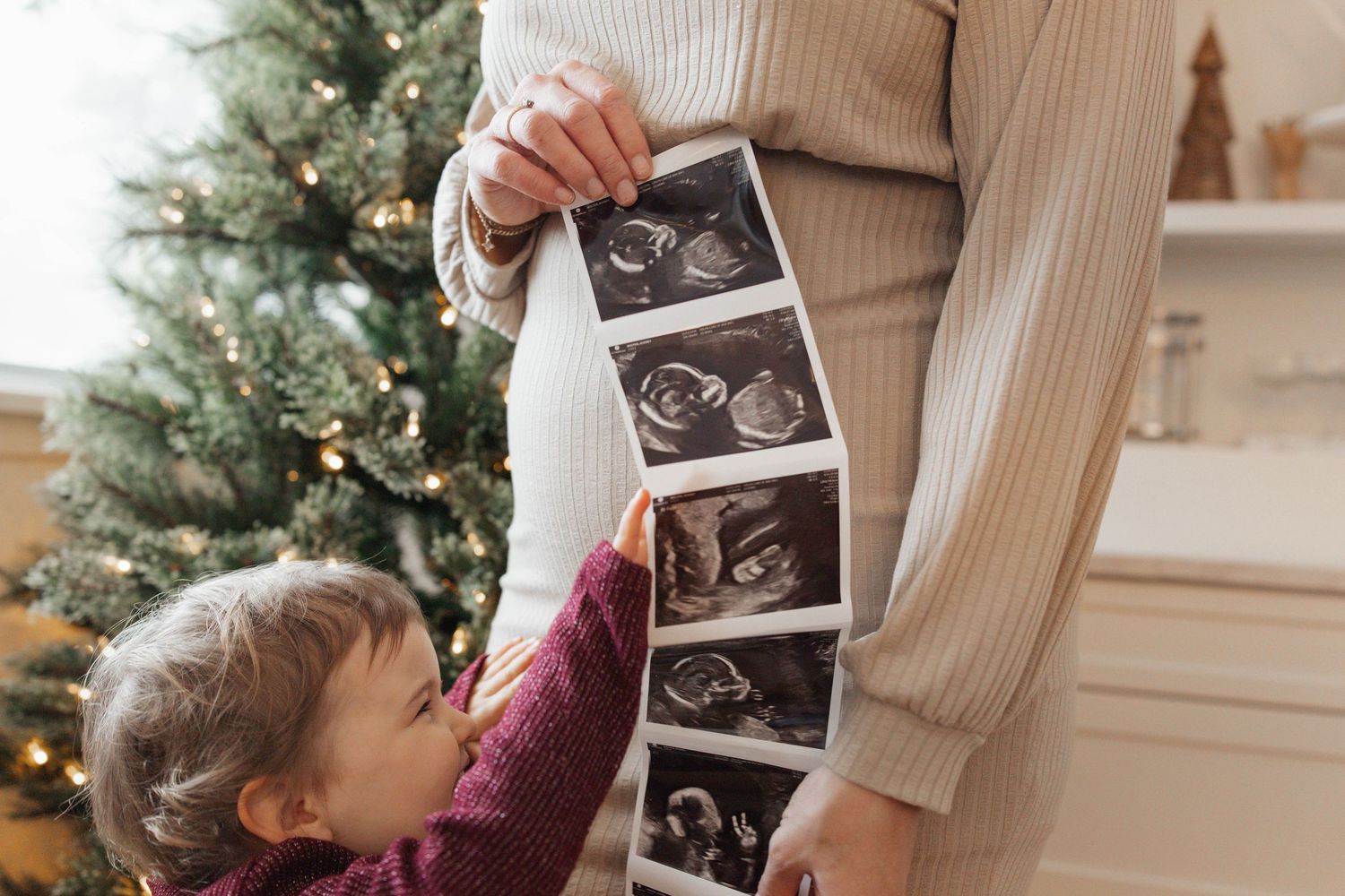 A series of ultrasound photos being held up in front of a decorated Christmas tree.