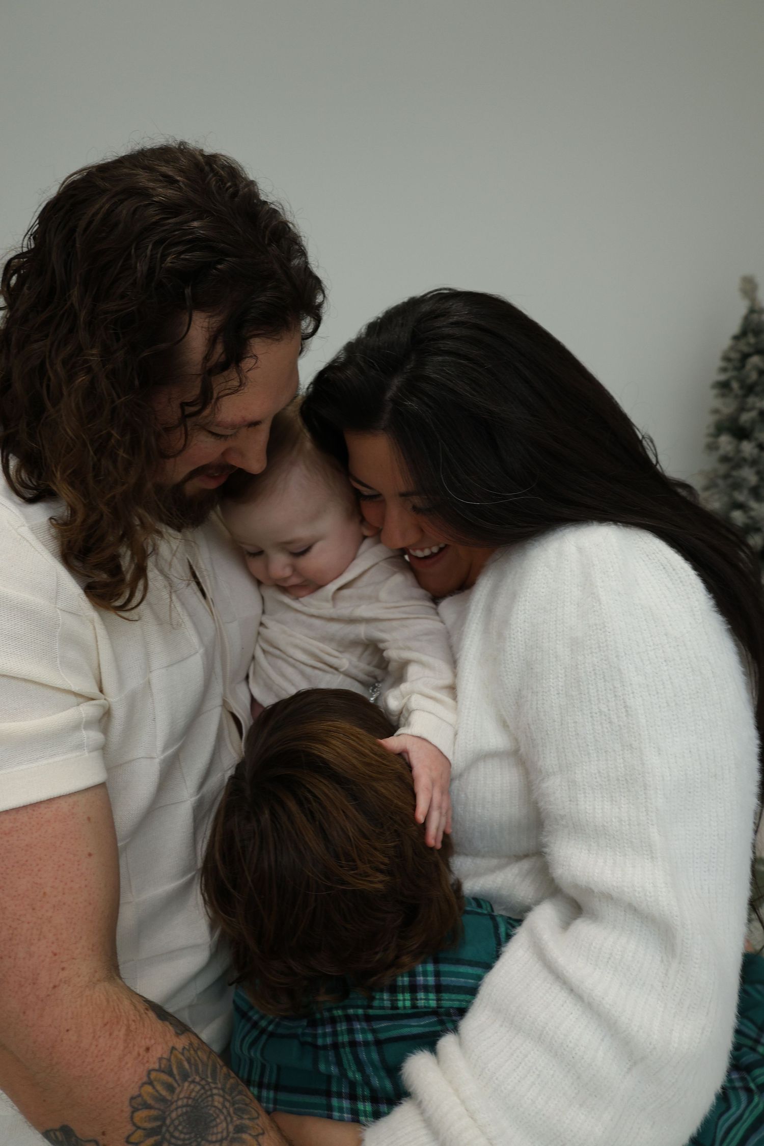 A family shares an intimate moment together, embracing in white sweaters while looking down at their young child.