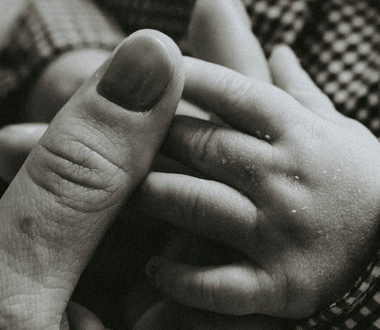 Black and white close-up of an adult hand gently holding a newborn baby's tiny hand.