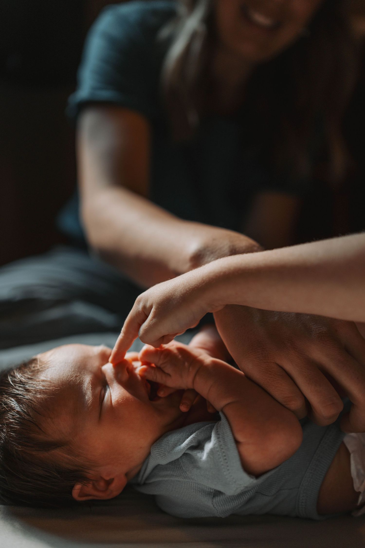 Smiling mother gently touching her newborn baby's nose as infant lies on back in soft natural light.