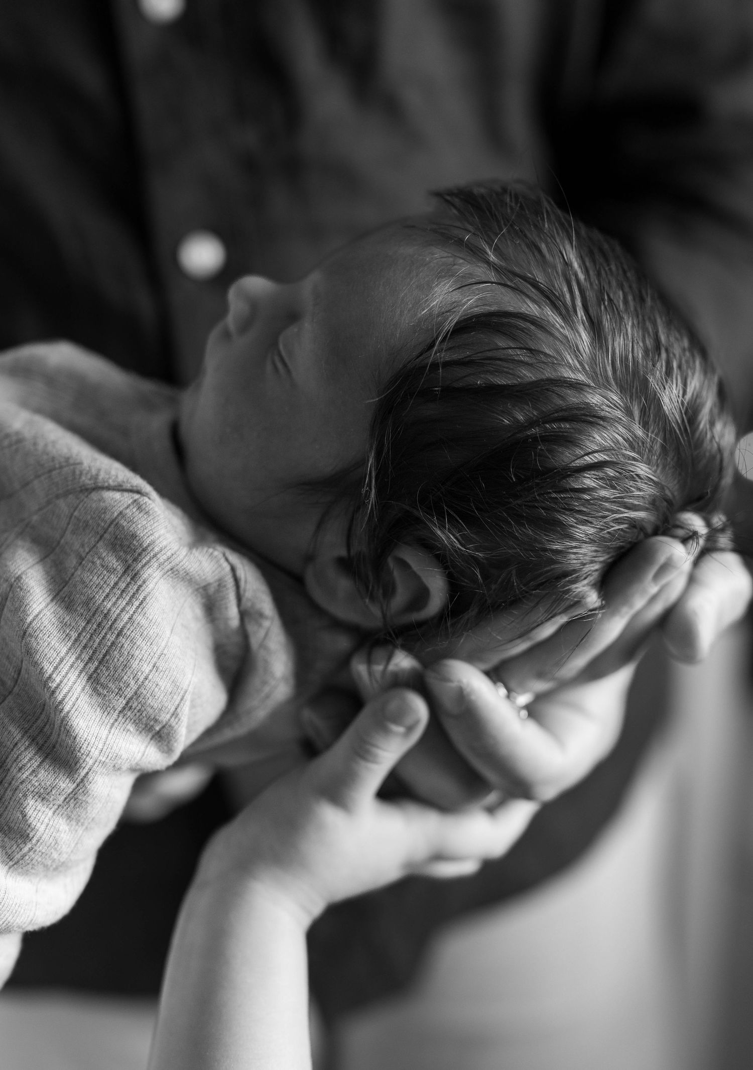 Close-up black and white photo of a newborn baby cradled in loving hands with a toddlers small hand nearby.