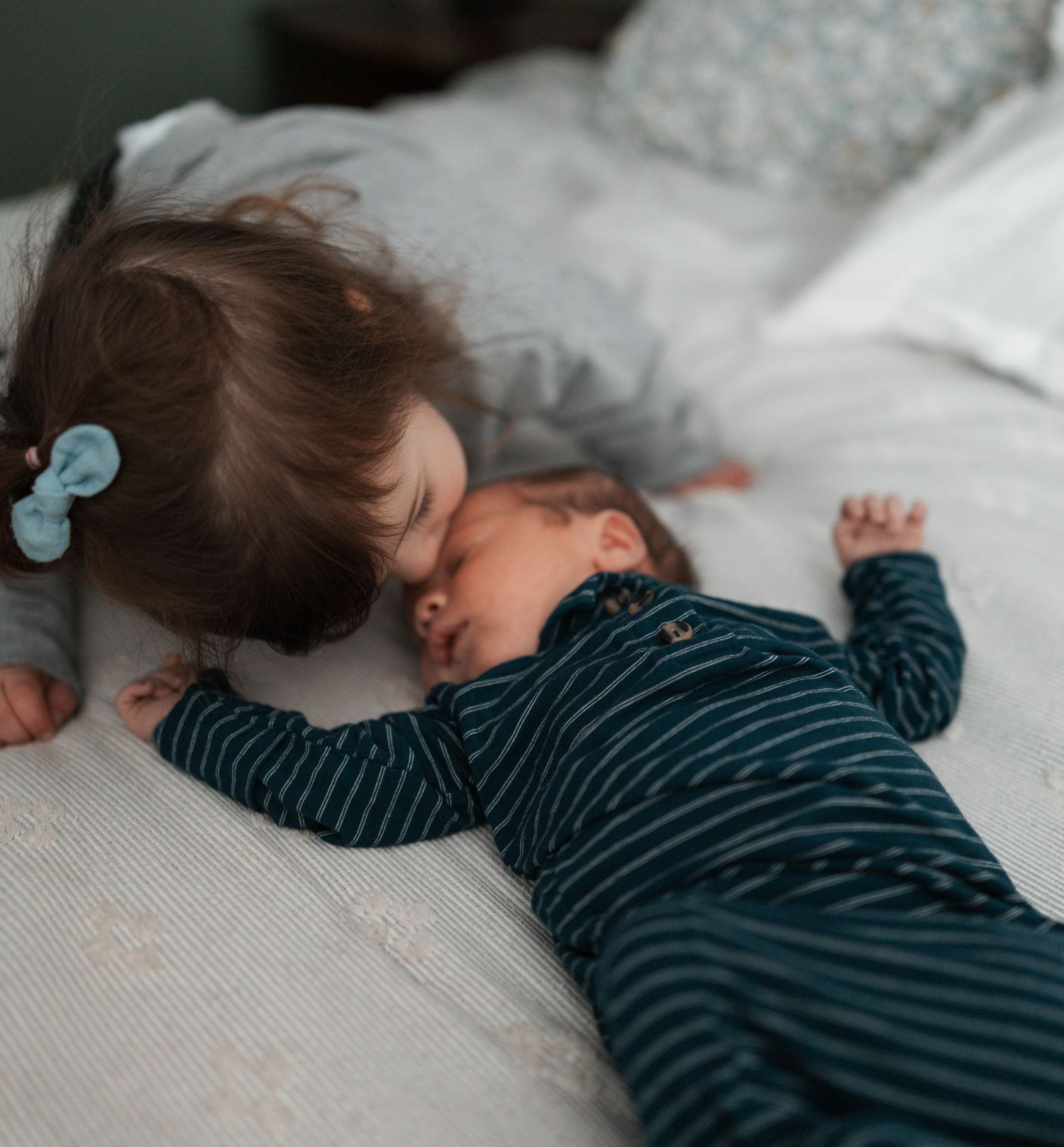 Two children sleeping peacefully on white bedding, one wearing a navy striped shirt.
