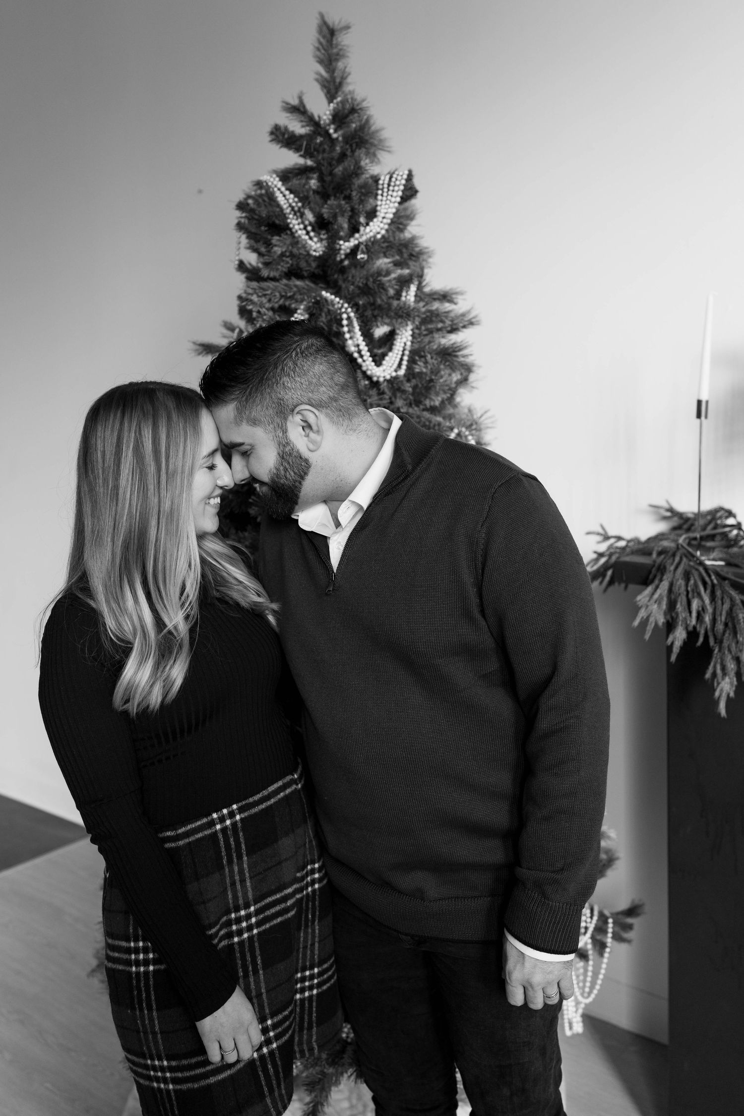 Black and white photos of couple in coordinated outfits posing intimately in front of a decorated Christmas tree.