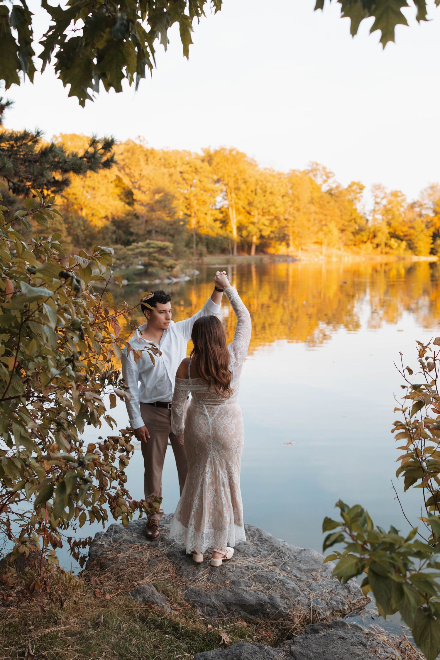 A couple dances together at sunset by a tranquil lake surrounded by golden autumn foliage.