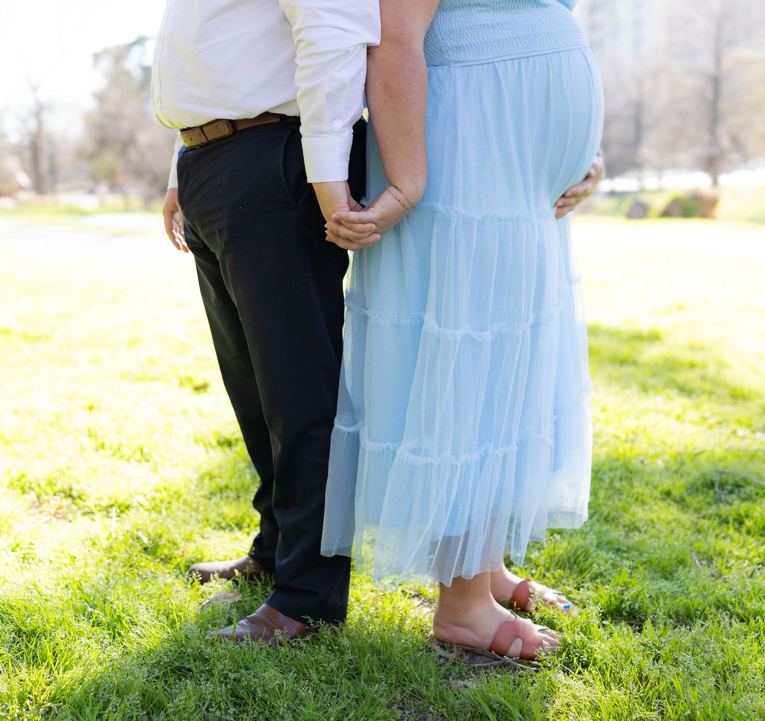 Close-up view of two people standing together on grass, showing blue tulle skirt and black pants.