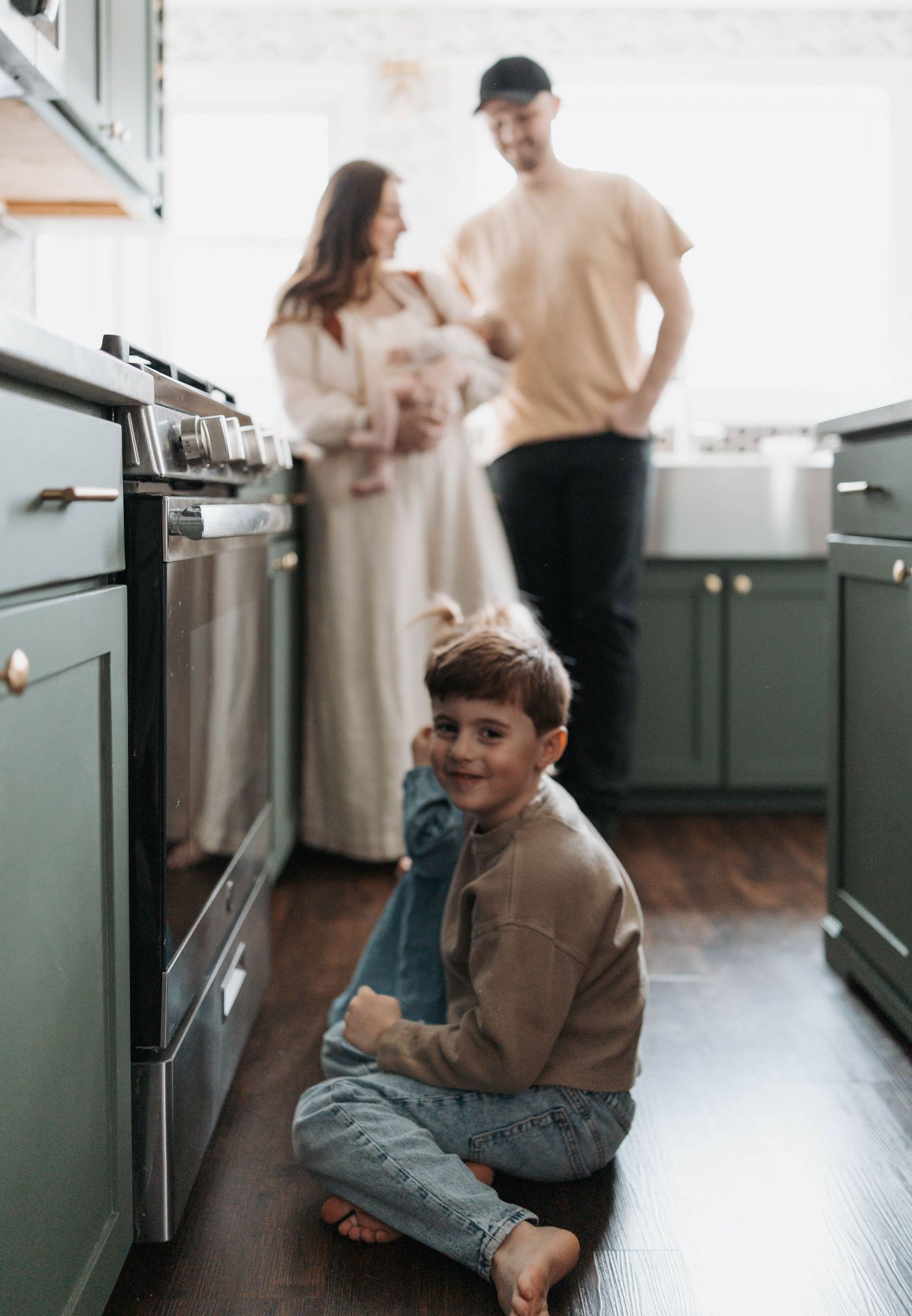 A candid family moment captured in a modern kitchen with green cabinets and hardwood floors.