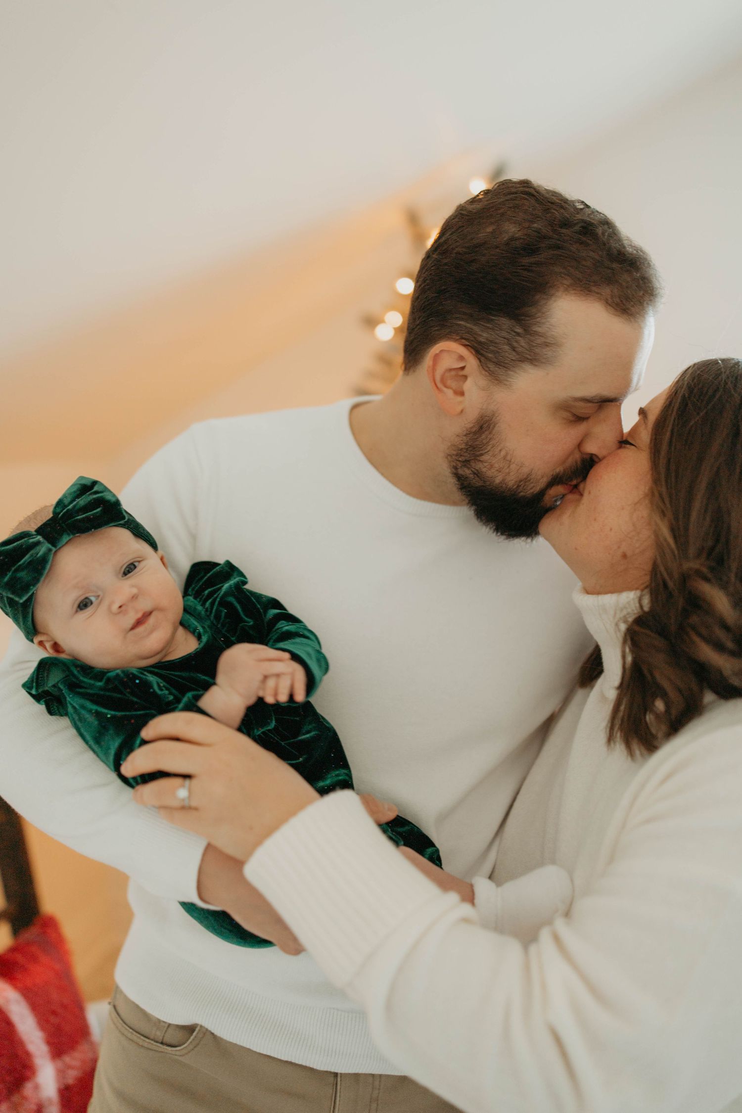 Sweet family moment captured as parents share a kiss while holding their baby dressed in green velvet.