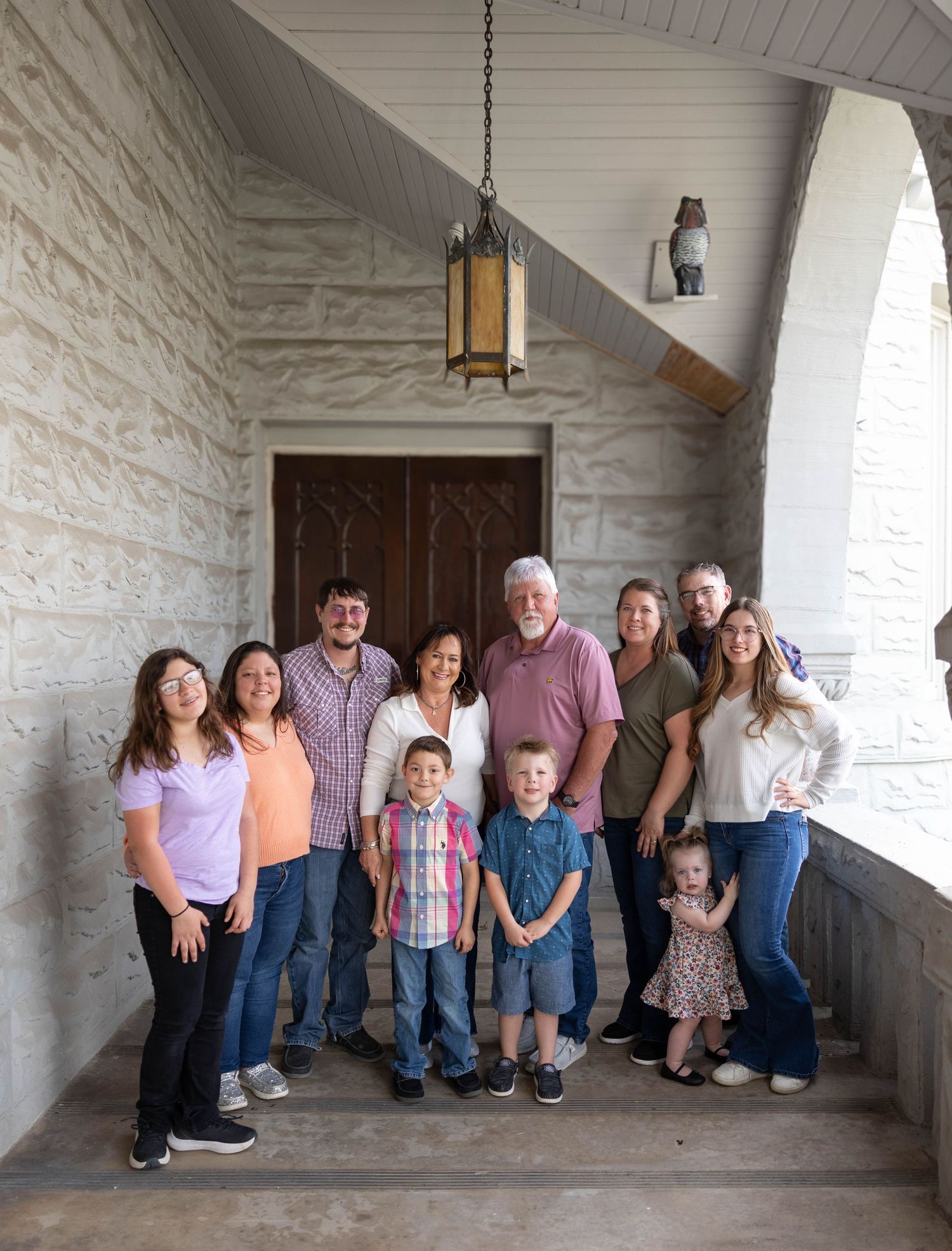 A family group poses for a portrait in a covered stone walkway with an overhead lantern and white walls.