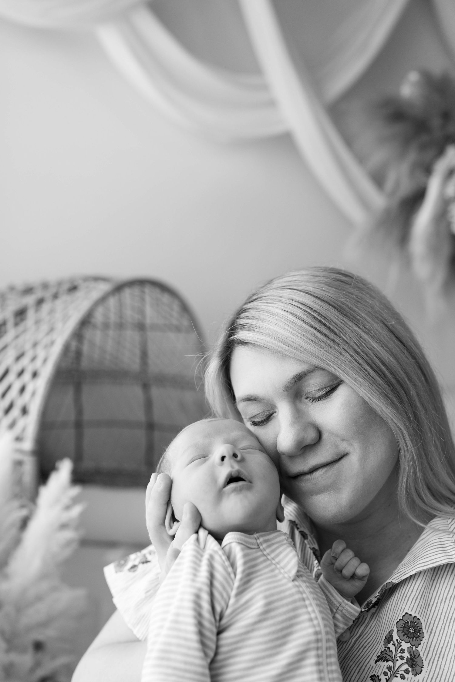 A tender black and white portrait showing a peaceful moment between parent and newborn baby in intimate embrace.