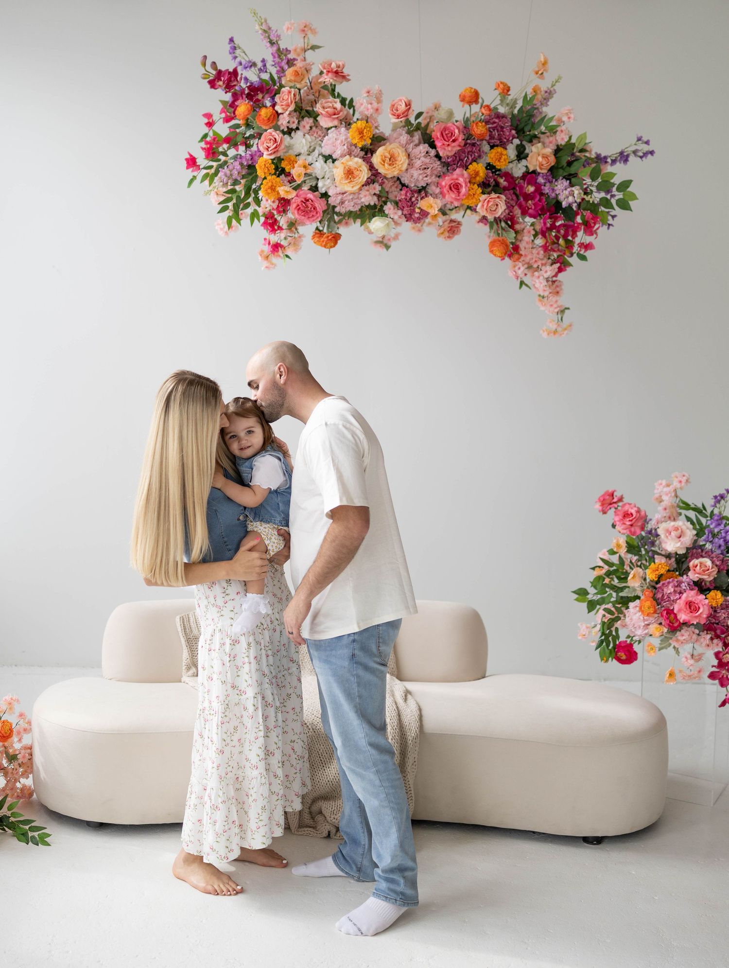 A modern minimalist indoor scene with a lavish floral arrangement above a beige sofa, decorated with pink and orange blooms.
