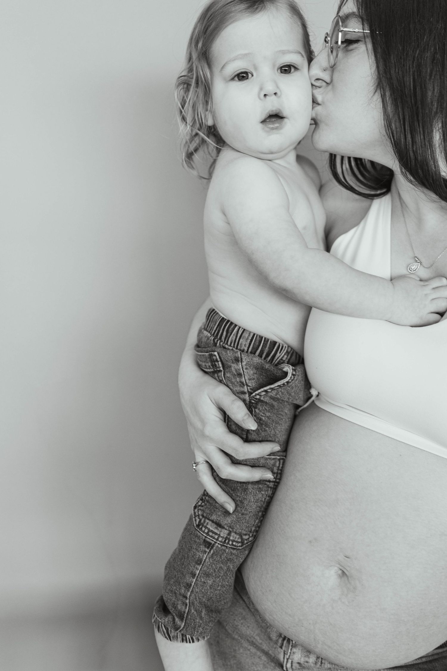 A tender black and white portrait showing a gentle kiss while holding a child against a pregnant belly.