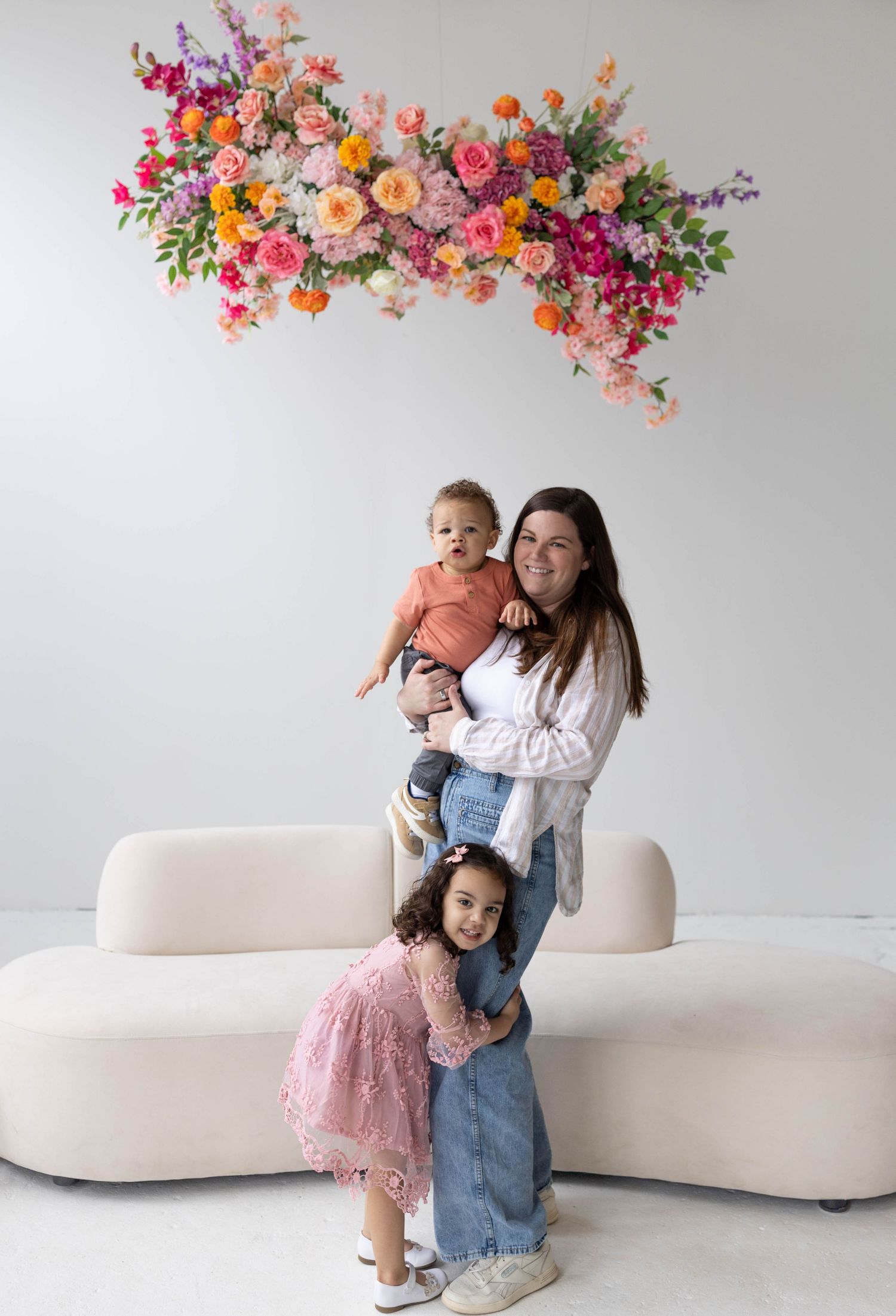 A vibrant floral installation with pink, peach and purple blooms hangs above a modern cream-colored curved sofa.