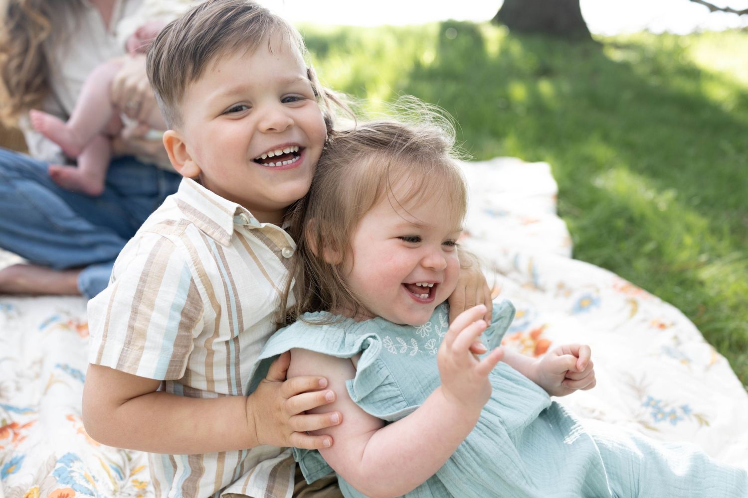 Children laughing and playing together while sitting on a blanket outdoors in the sunshine.