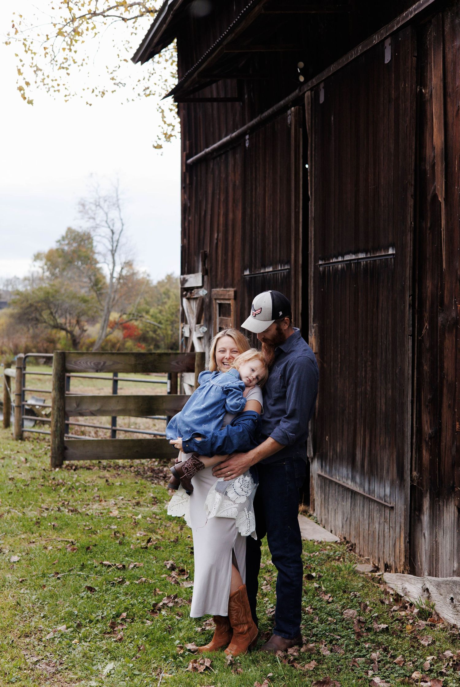 Romantic countryside photoshoot against weathered wooden barn with rustic fencing in autumn.