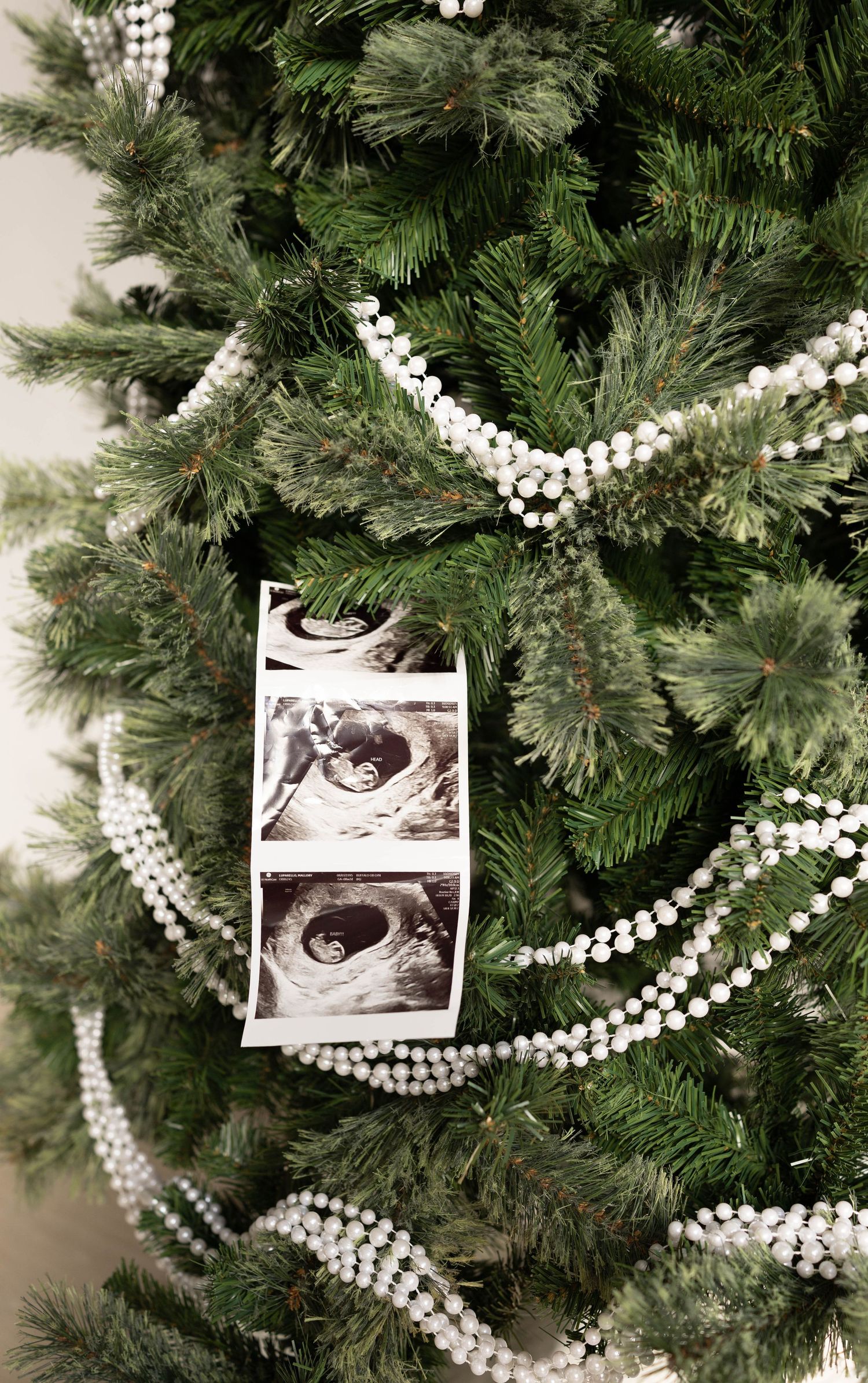 Christmas tree decorated with white beaded garland and black and white ultrasound photos hanging as ornaments.