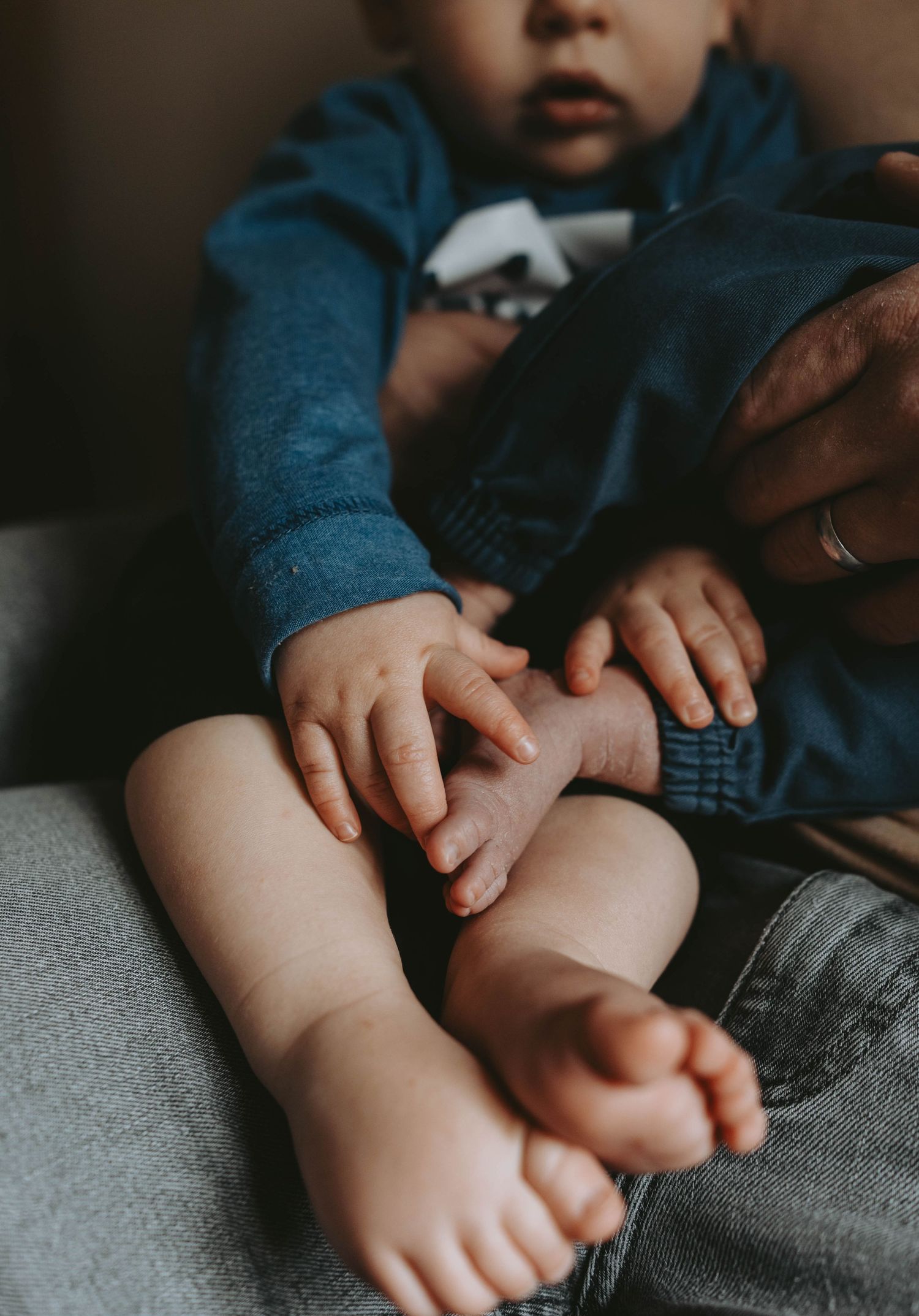 Close-up of a baby's tiny hands and bare feet resting on an adult's lap in a cozy home setting.